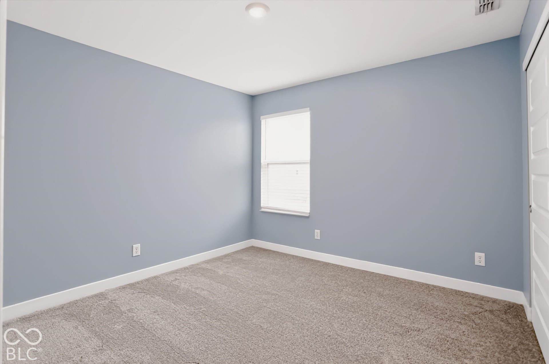 Neutral-toned interior space featuring light blue wall paint, wall-to-wall carpeting, a single-window configuration, and a multi-panel door