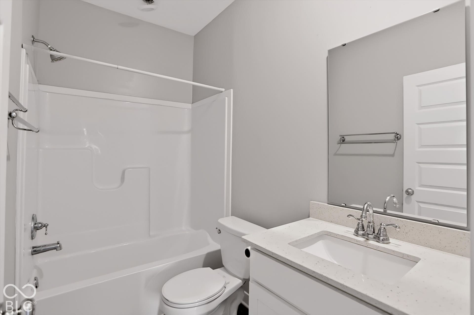 Bathroom featuring a white vanity with a composite countertop, undermount sink, chrome faucet, wall-mounted mirror, and a tub-shower combination with a surround