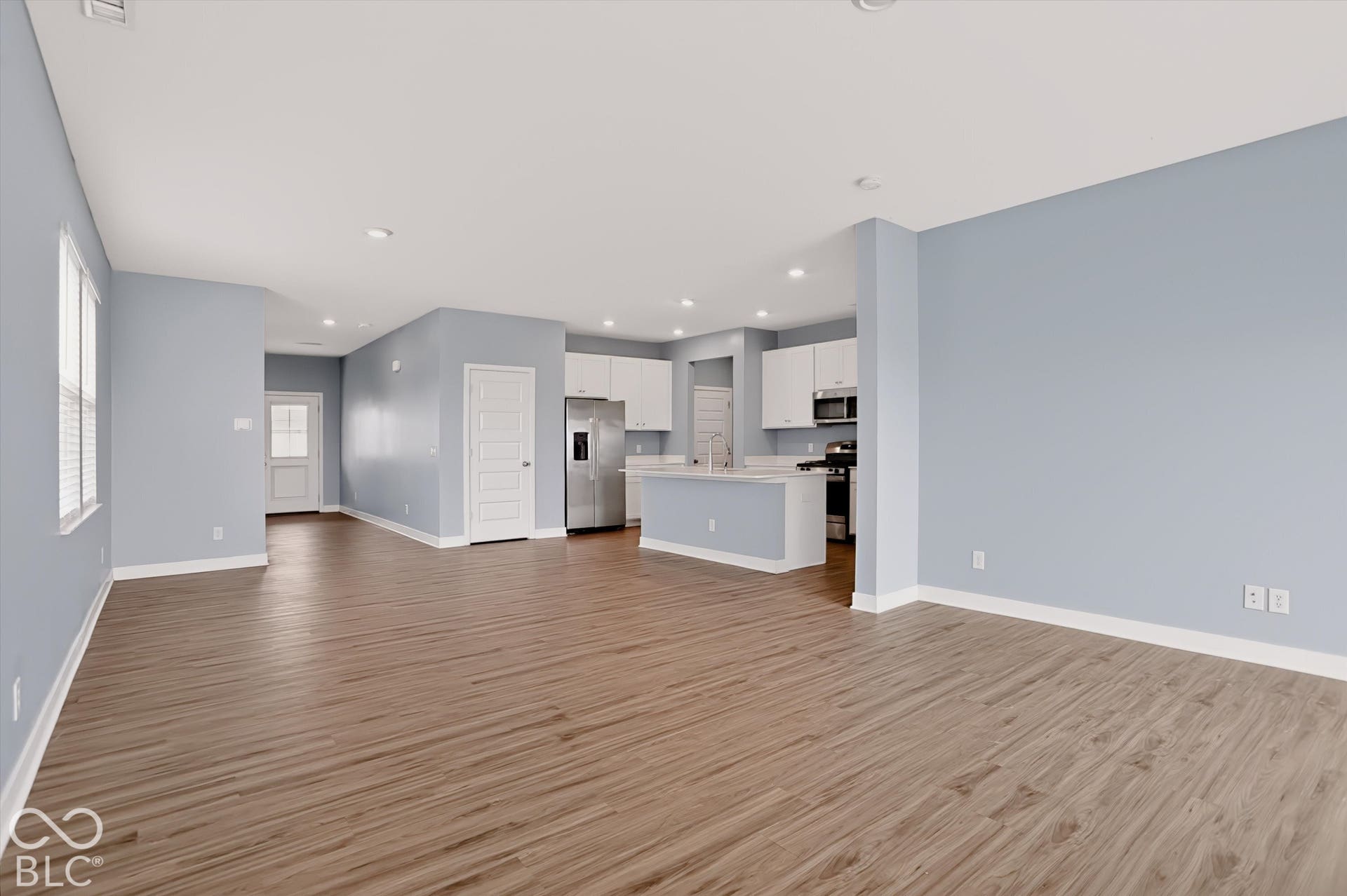 Open-concept floor plan featuring wood-finish flooring, recessed lighting, white cabinetry, a kitchen island, and stainless steel appliances