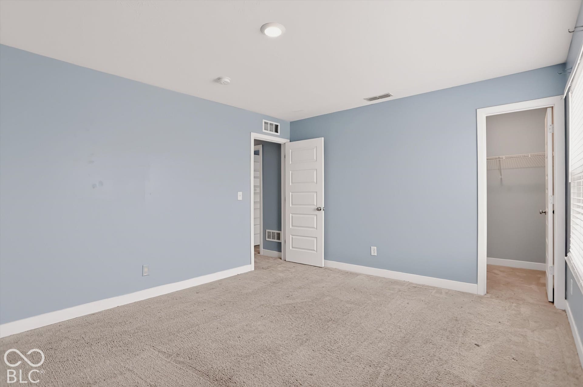 Neutral-toned wall paint, recessed lighting, carpeted flooring, five-panel interior door, and walk-in closet with built-in wire shelving