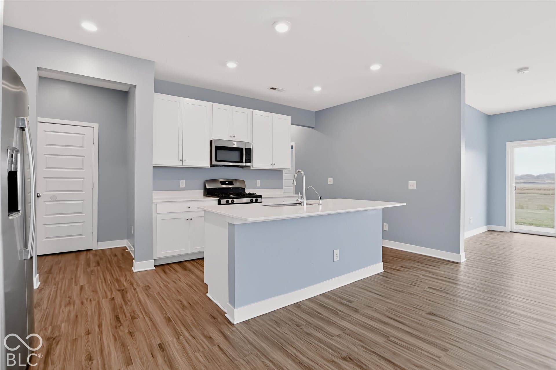 Kitchen featuring white cabinetry, solid-surface countertops, center island with an integrated sink, stainless steel appliances, and wood-finish flooring