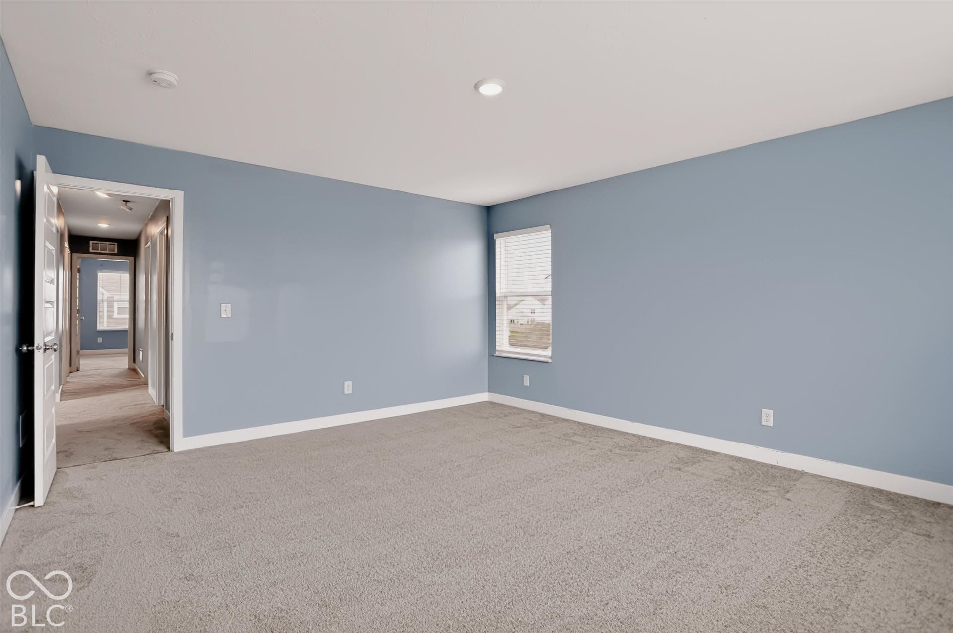 Interior space featuring neutral-toned carpeting, light blue wall paint, a single window with blinds, and recessed lighting