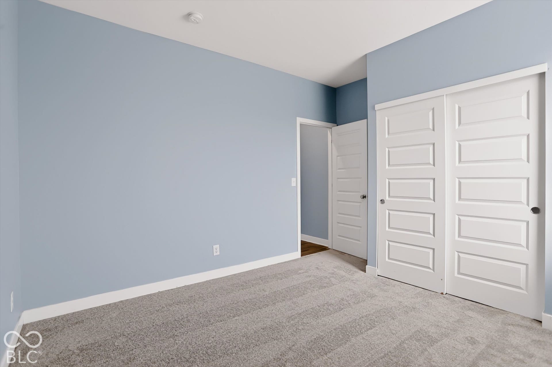 Room featuring neutral carpeting, light blue wall paint, and a sliding-door closet with five-panel door detailing