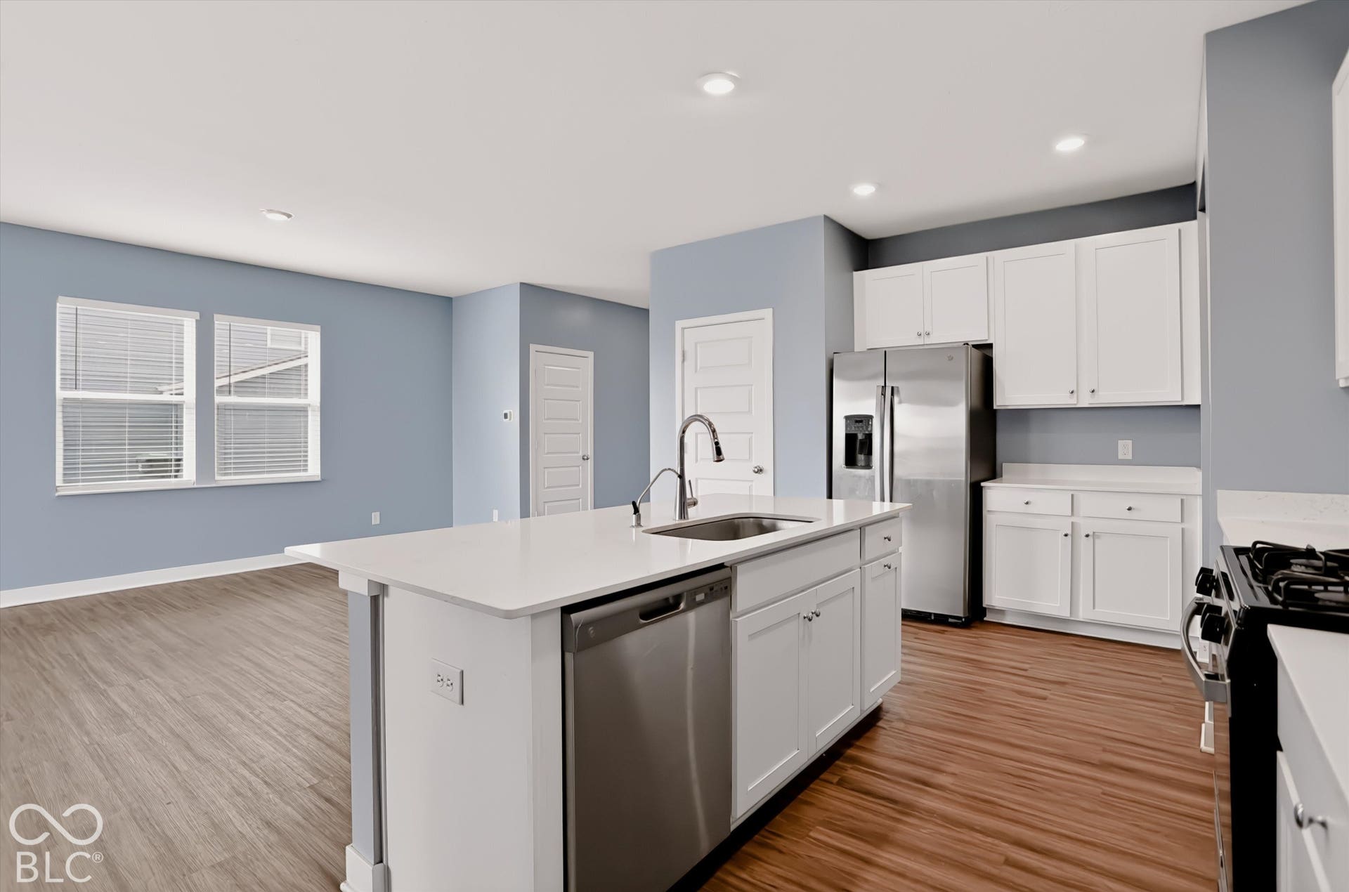 Kitchen featuring white cabinetry, center island with stainless steel dishwasher, stone-finish countertops, stainless steel refrigerator, and wood-finish flooring