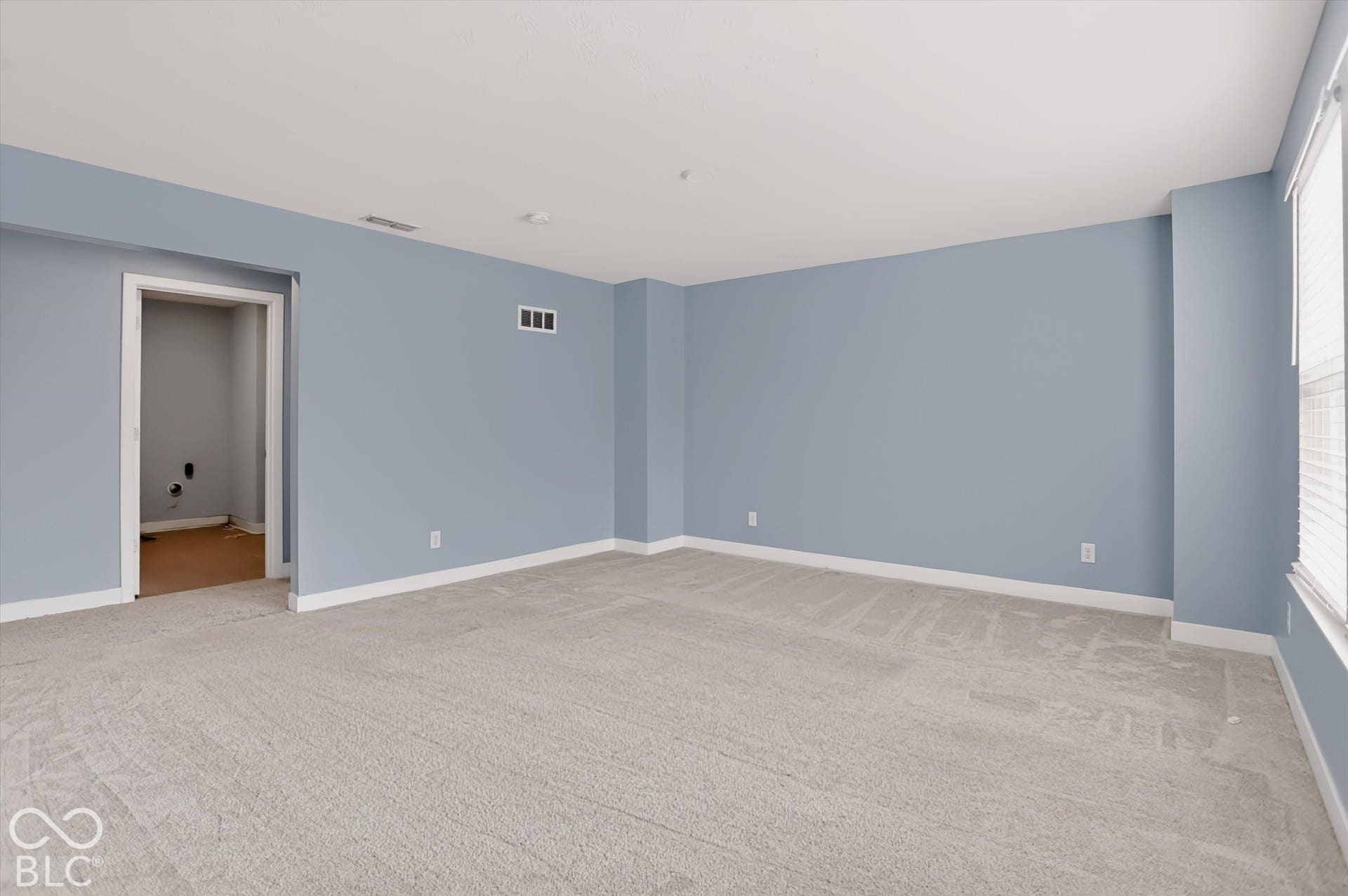 Spacious room featuring neutral carpeting, light-toned wall paint, and windows with integrated blinds