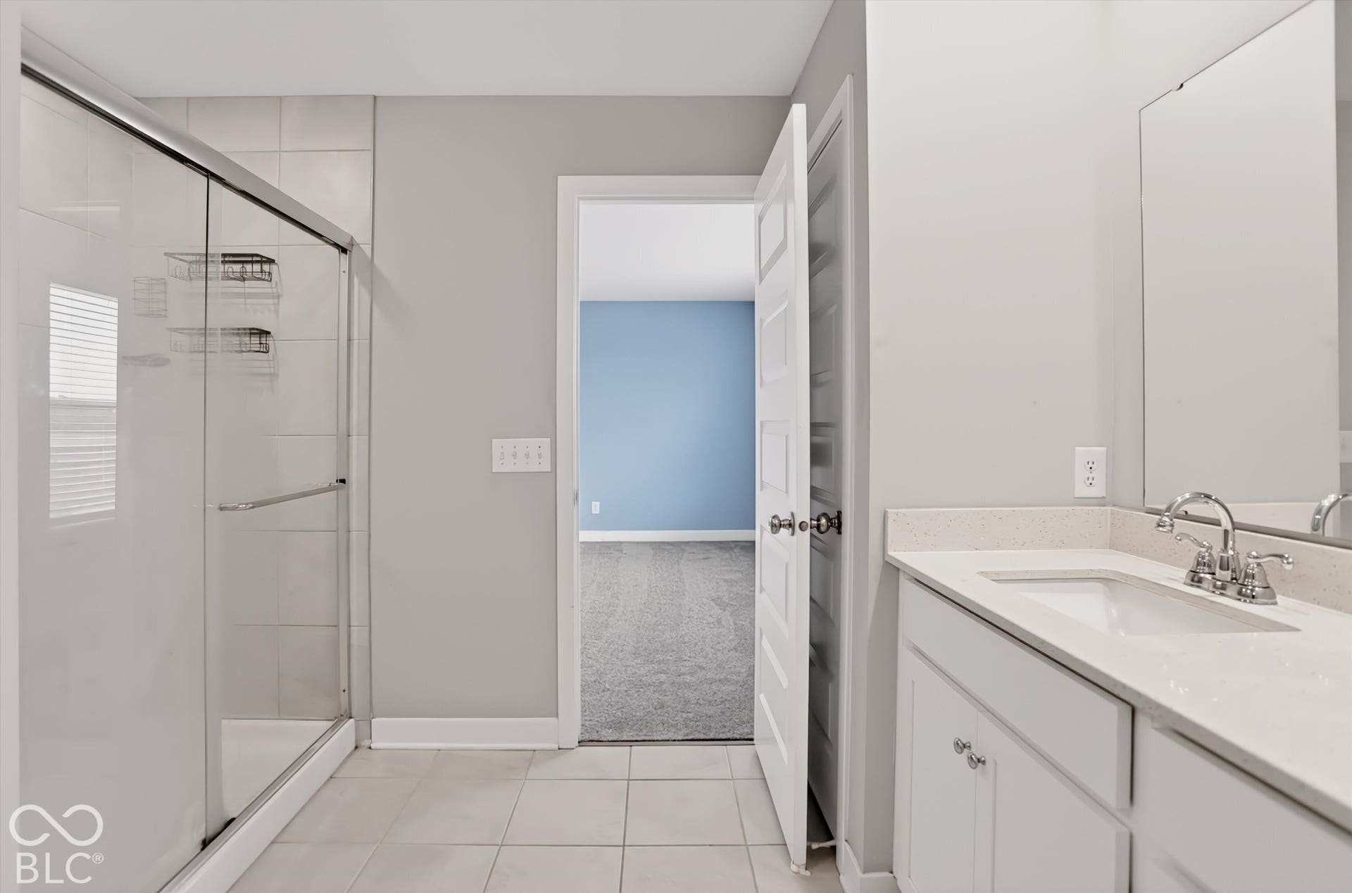 Bathroom featuring a shower stall with a glass enclosure, white vanity with stone-composite countertop, undermount sink, and tile flooring