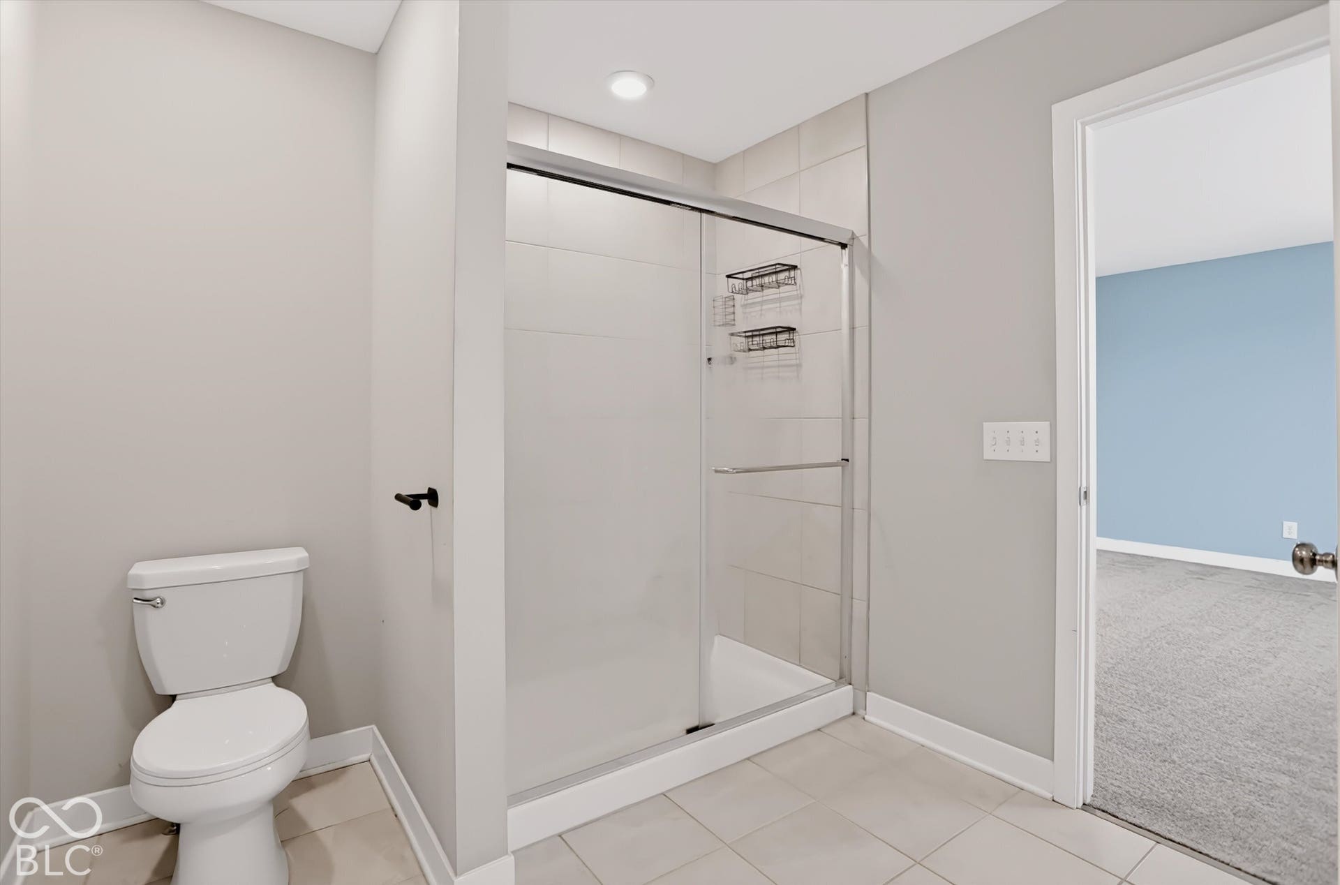Shower enclosure featuring sliding glass doors, neutral tile surround, and built-in shelving, complemented by ceramic tile flooring and a standard-height toilet