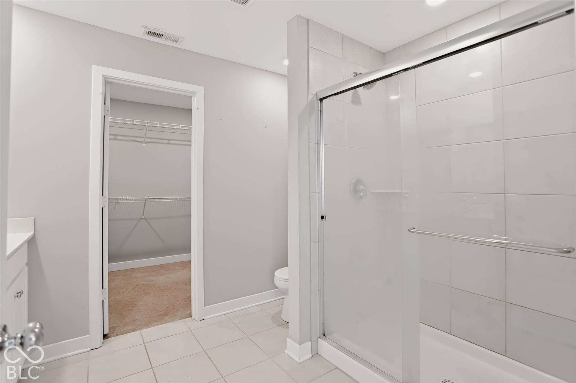 Shower with large-format wall tile and glass sliding door, porcelain tile flooring, built-in vanity with solid surface countertop, and walk-in closet with built-in shelving