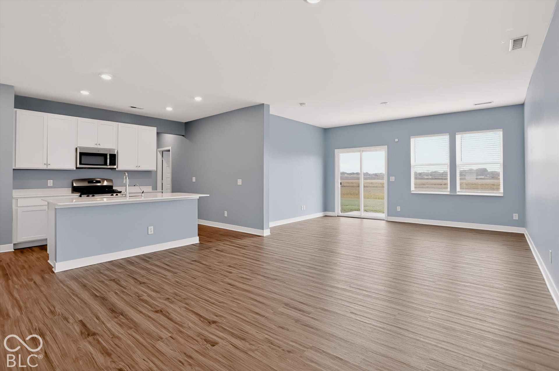 Open-concept area featuring wood-finish flooring, white cabinetry, a center island with a stone-surfaced countertop, recessed lighting, and a sliding glass door