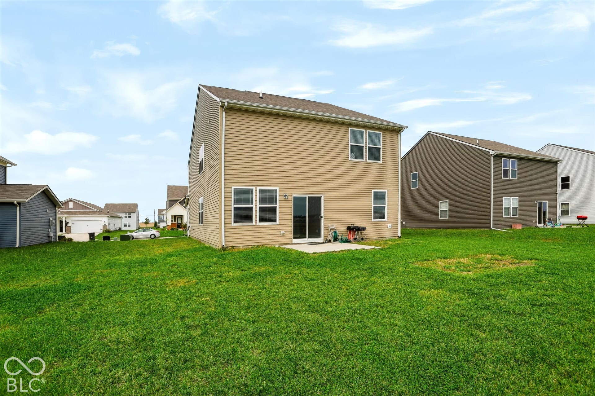 Two-story residence featuring light-toned horizontal siding, a concrete rear patio, sliding glass door, and a grass-covered backyard