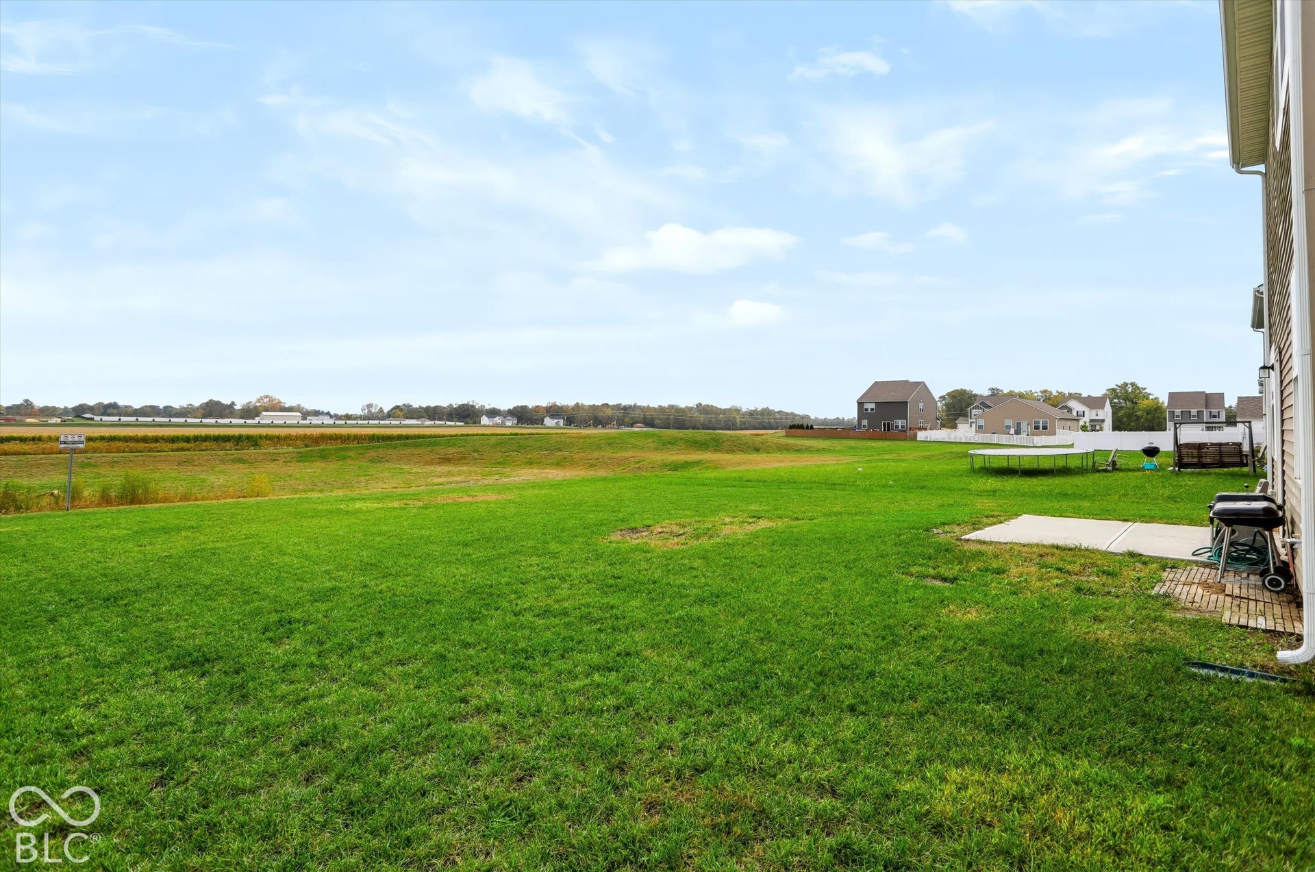 Expansive backyard featuring a large grass lawn, concrete patio, and open field perimeter