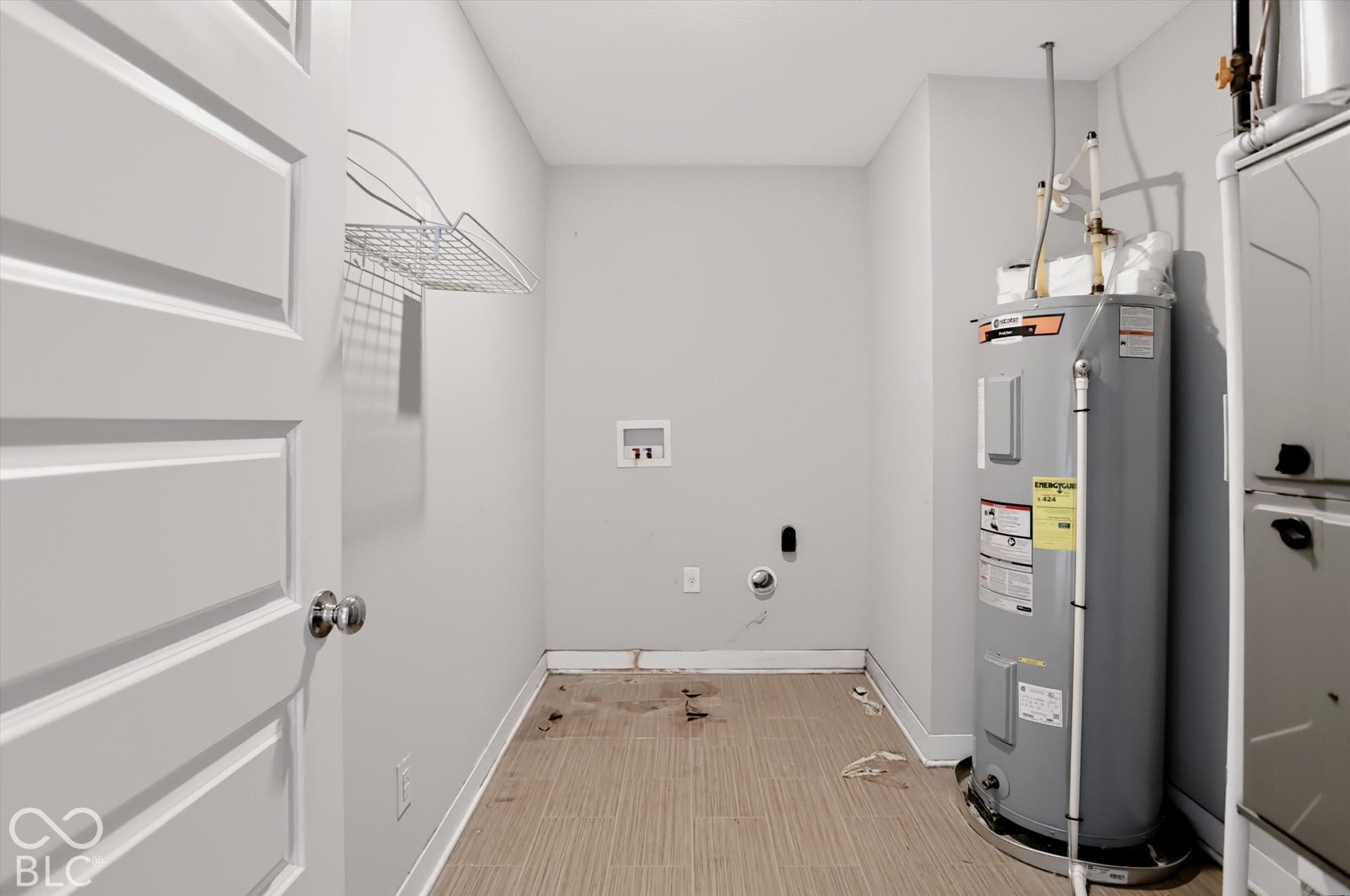 Utility area featuring a wall-mounted wire storage shelf, dedicated washer and dryer hookups, tile flooring, and an integrated water heater