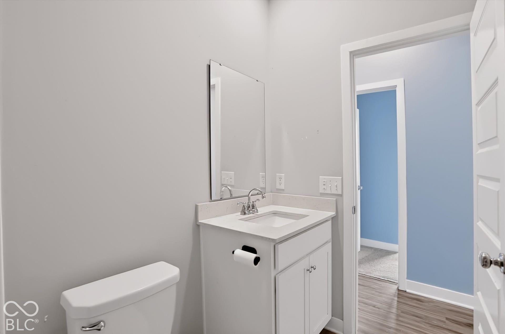 Bathroom featuring a white vanity cabinet, solid-surface countertop with an integrated rectangular sink, wall-mounted mirror, and chrome faucet hardware