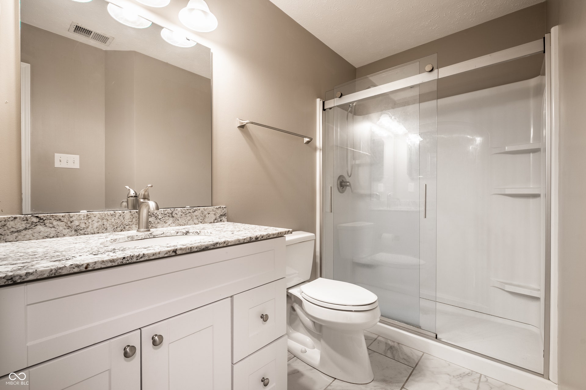 Guest Bathroom featuring a white vanity with a light granite countertop, a large framed mirror, and a shower with sliding glass doors