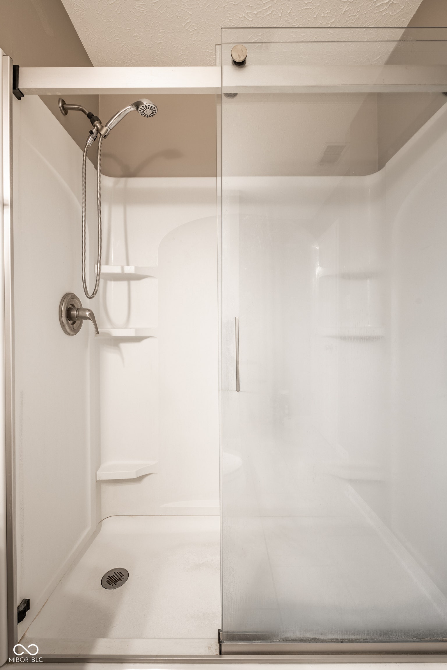 Guest bath.  Shower enclosure featuring a sliding glass door, a built-in shower caddy, and a brushed nickel showerhead with a handheld spray