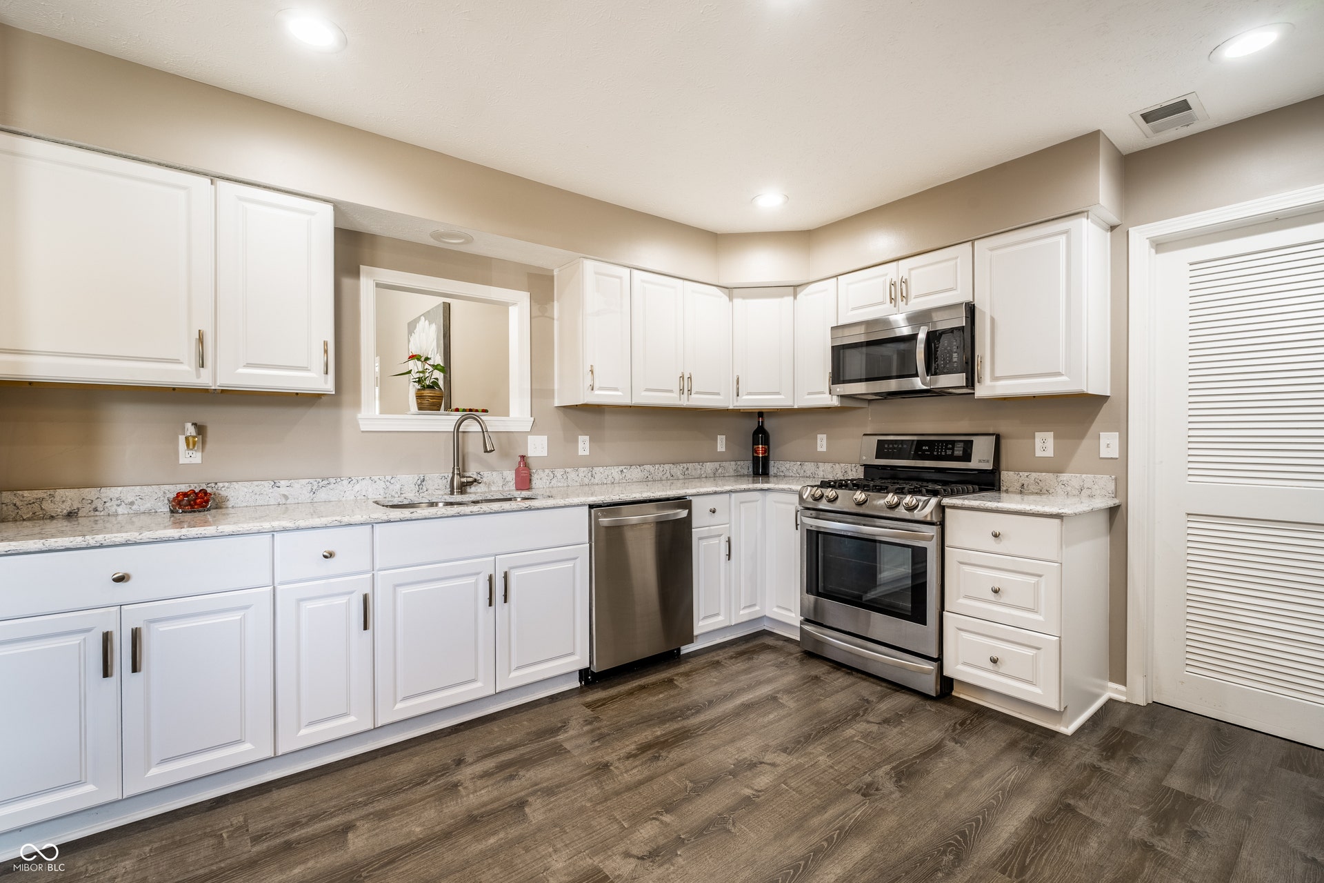 White cabinetry with brushed nickel hardware, stainless steel appliances, light-toned quartz kitchen countertops with ogee edgings, wood-finish flooring, and recessed lighting