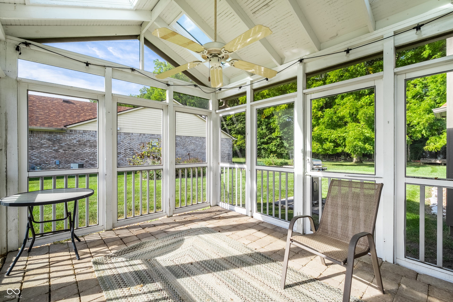 Screened porch featuring a skylight, ceiling fan, string lighting, and paver flooring