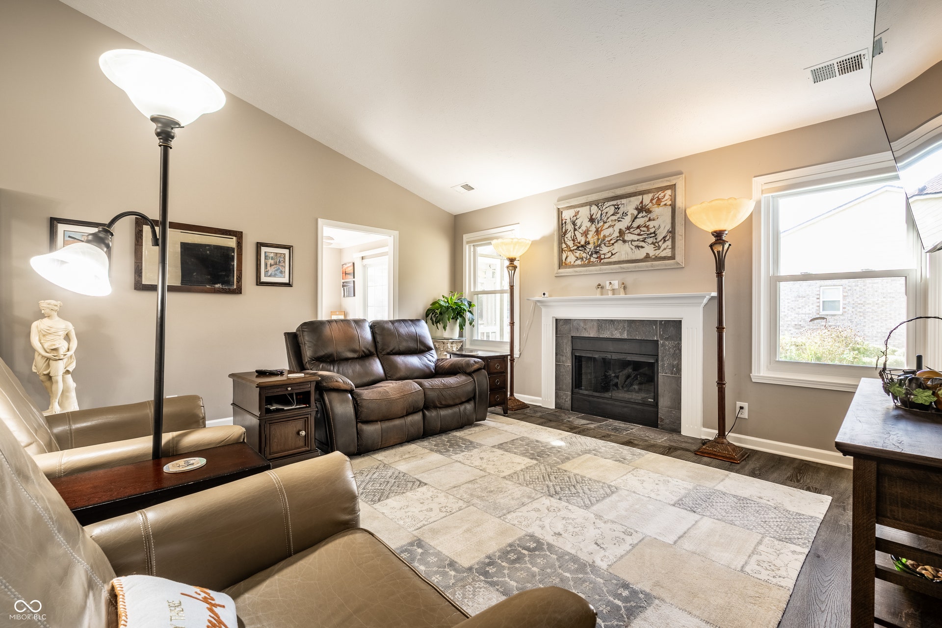 Vaulted ceiling with natural light, central fireplace with a slate surround and mantle, and wood-finish flooring