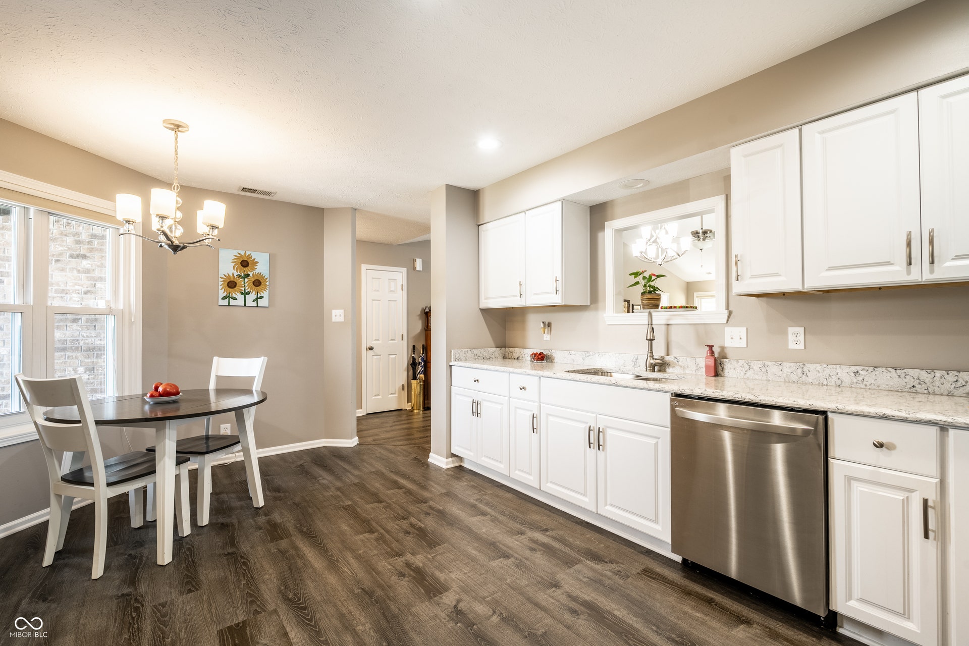 Bright, open-concept kitchen and dining area featuring white cabinetry with stainless steel hardware, quartz countertops, stainless steel appliances including a dishwasher, wood-finish flooring throughout, and abundant natural light from multiple win