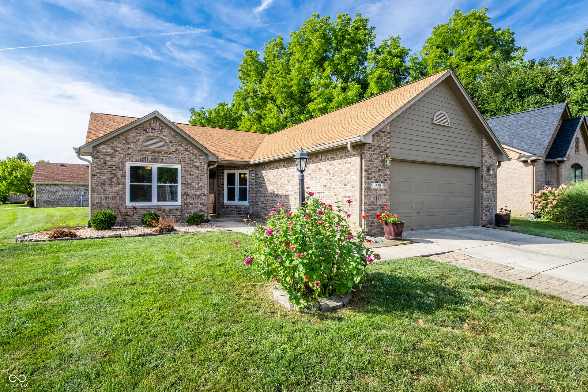 Brick exterior with light siding accents, two-car garage, front landscaping, and a paved driveway
