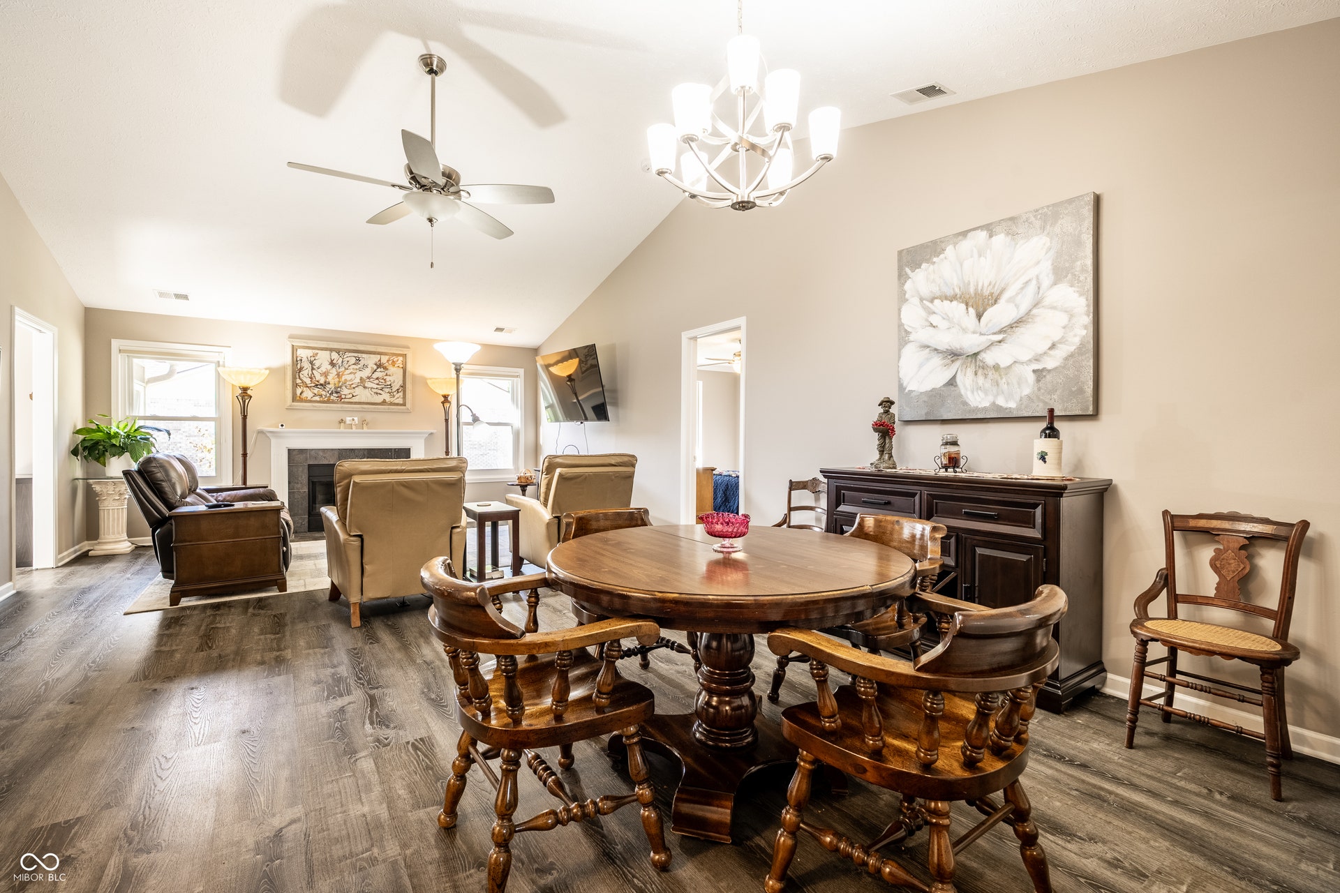 Vaulted ceilings, wood-finish flooring, a ceiling fan, and a chandelier illuminate this open space with a fireplace