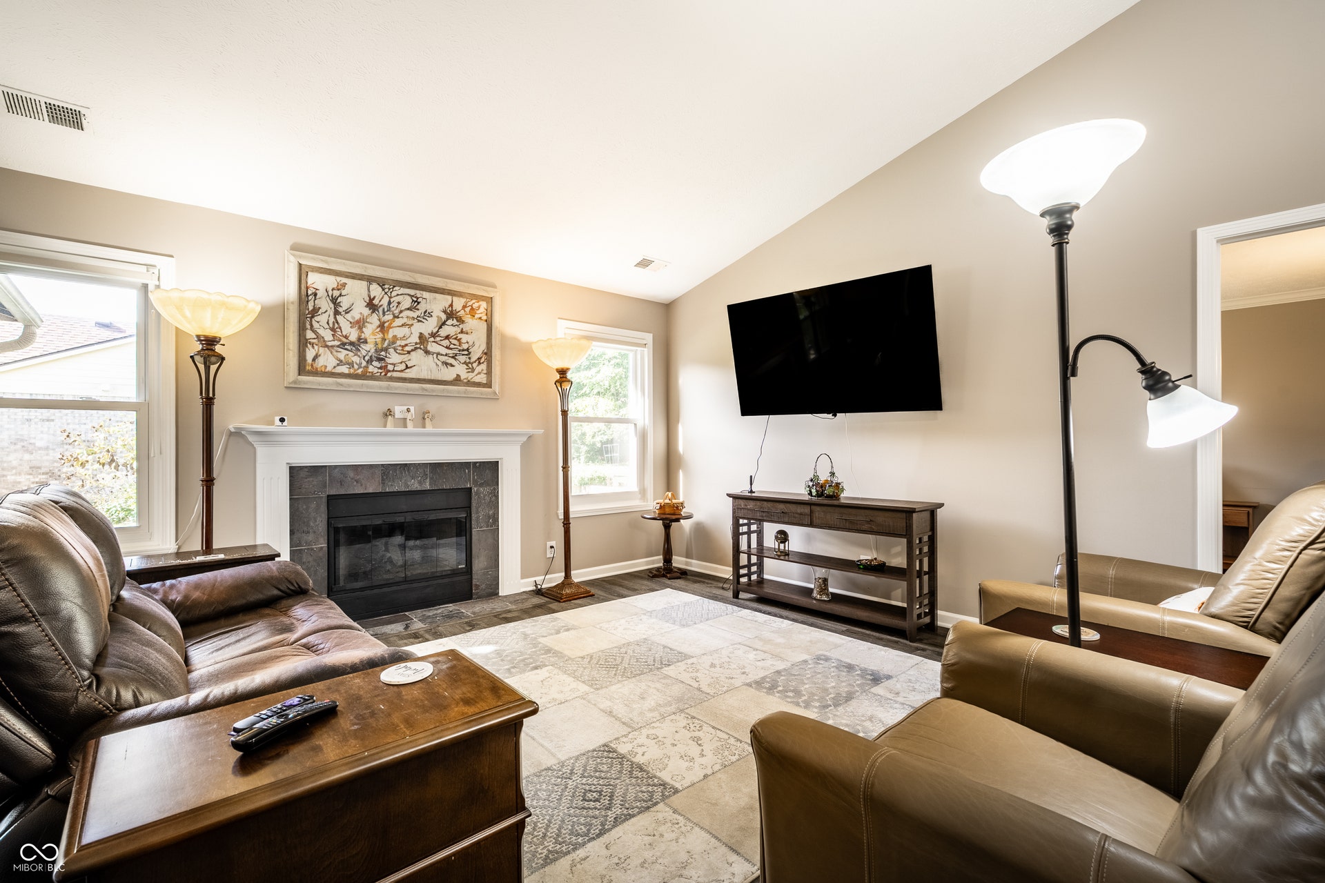 Vaulted ceiling with natural light, fireplace with slate surround, white mantel, and two windows with white trim. TV mount to convey with home
