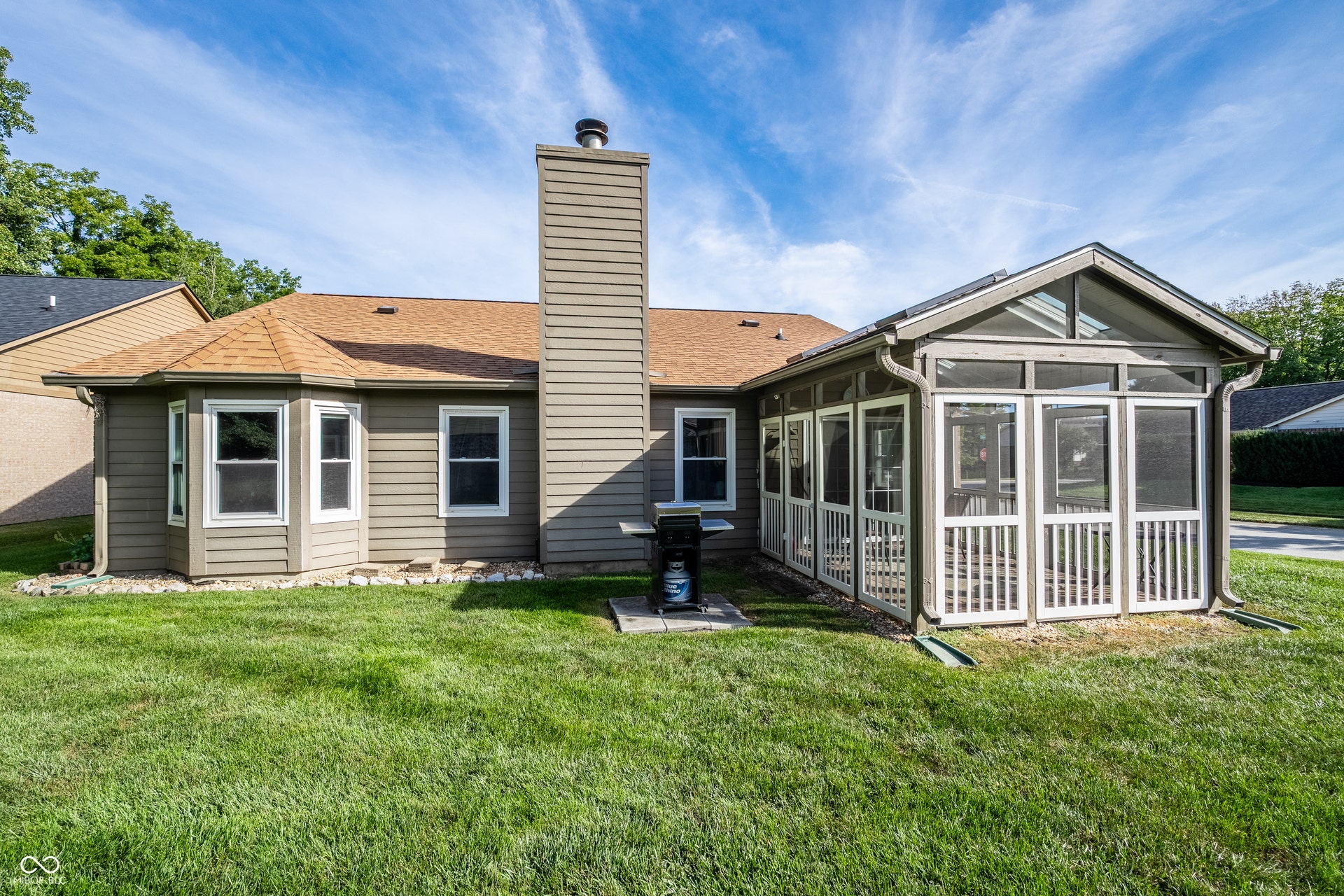 Expansive grassy yard with a screened-in porch, bay window, and a prominent exterior chimney