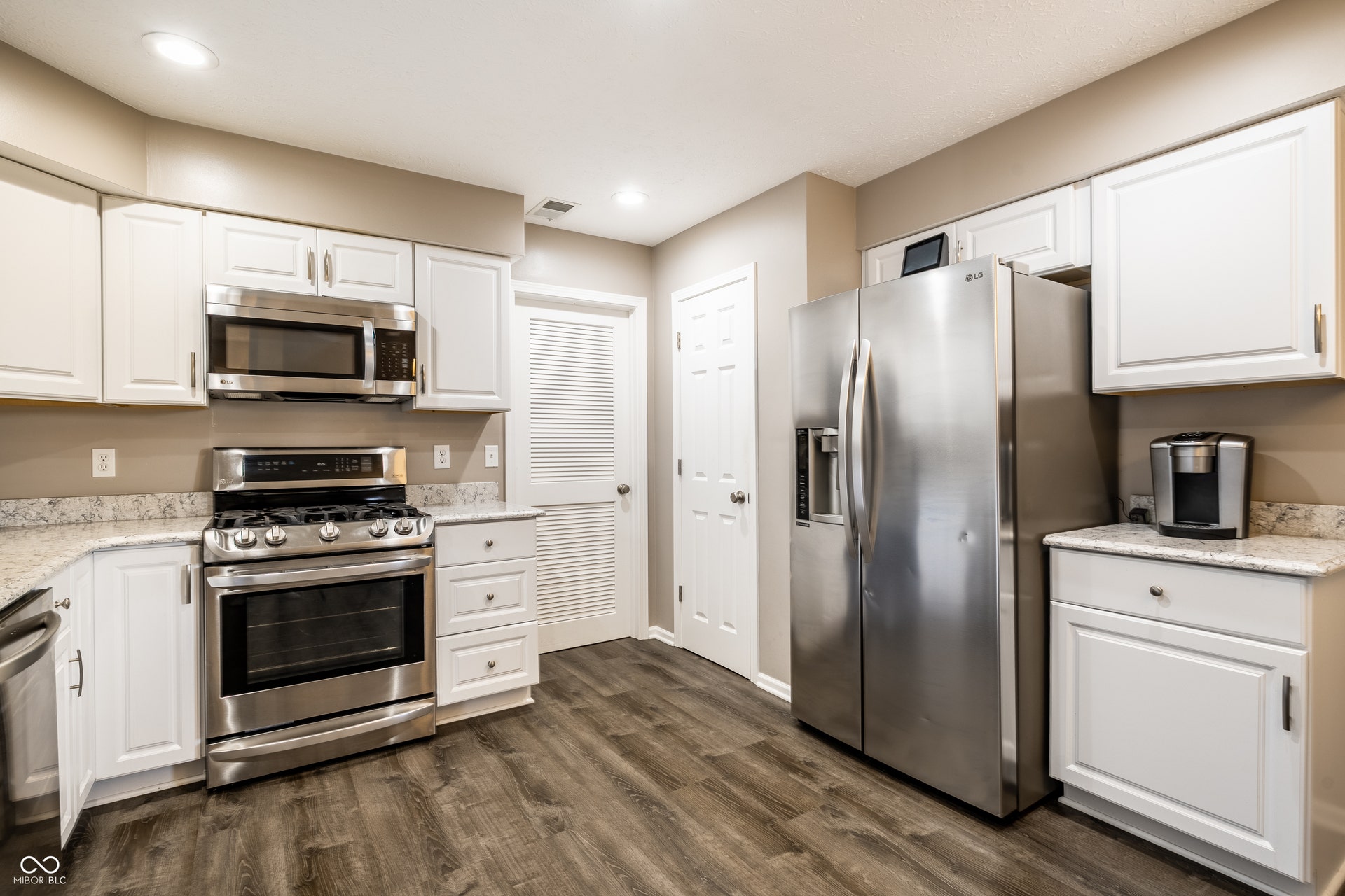 White cabinetry with stainless steel appliances, quartz countertops, wood-finish flooring, and recessed lighting
