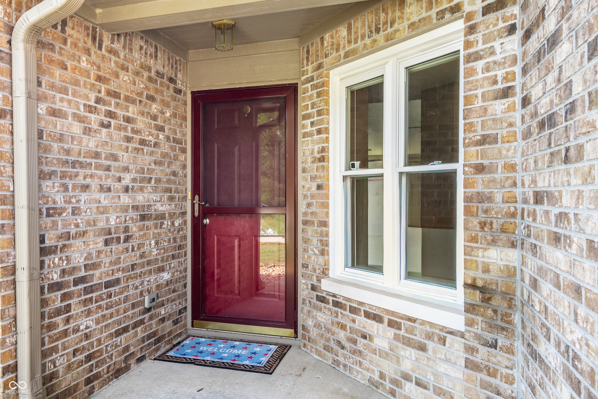 Brick exterior with a red entry door, storm door, and double-hung window