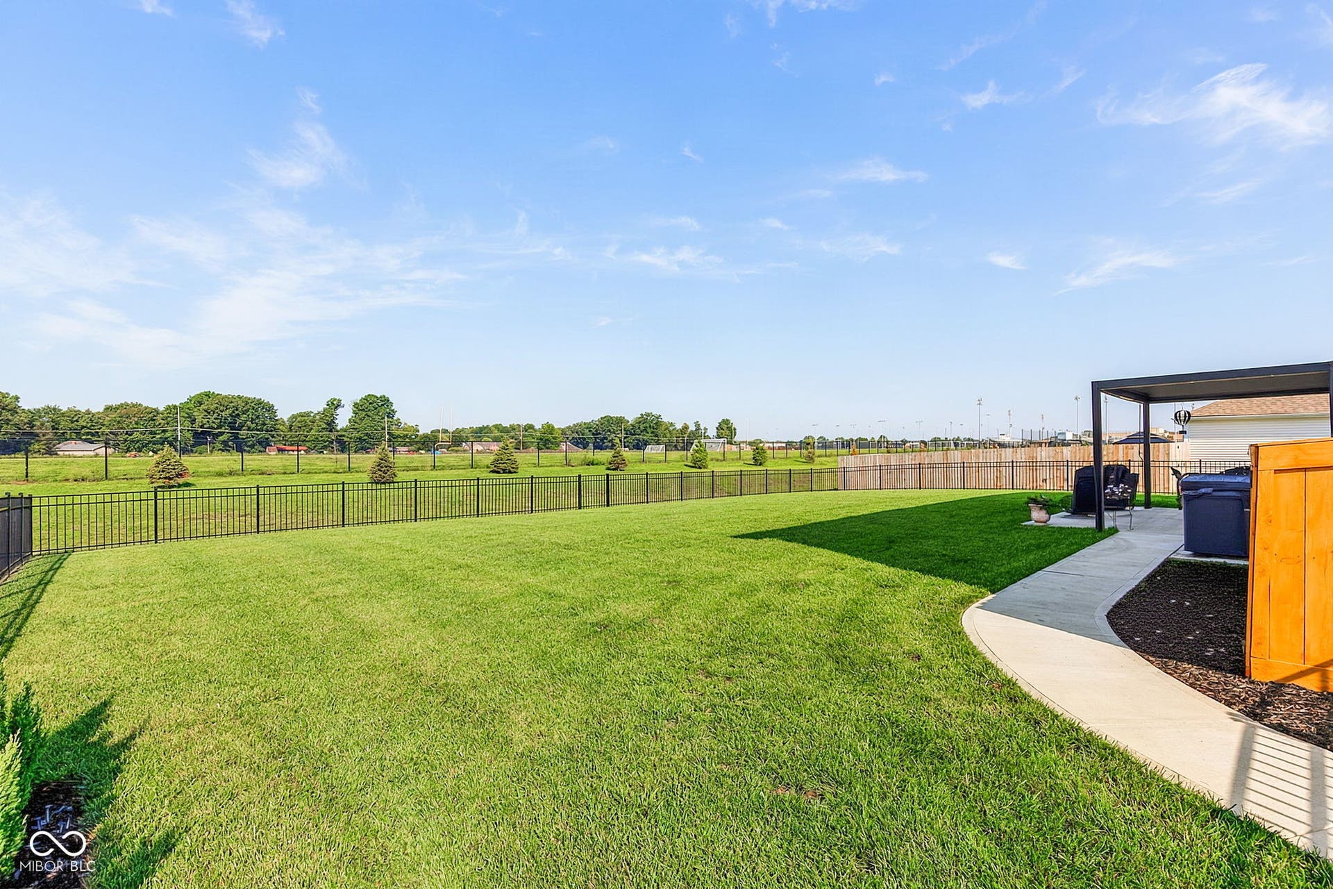 Expansive backyard featuring a lush lawn, black metal fencing, a concrete patio, and a modern pergola