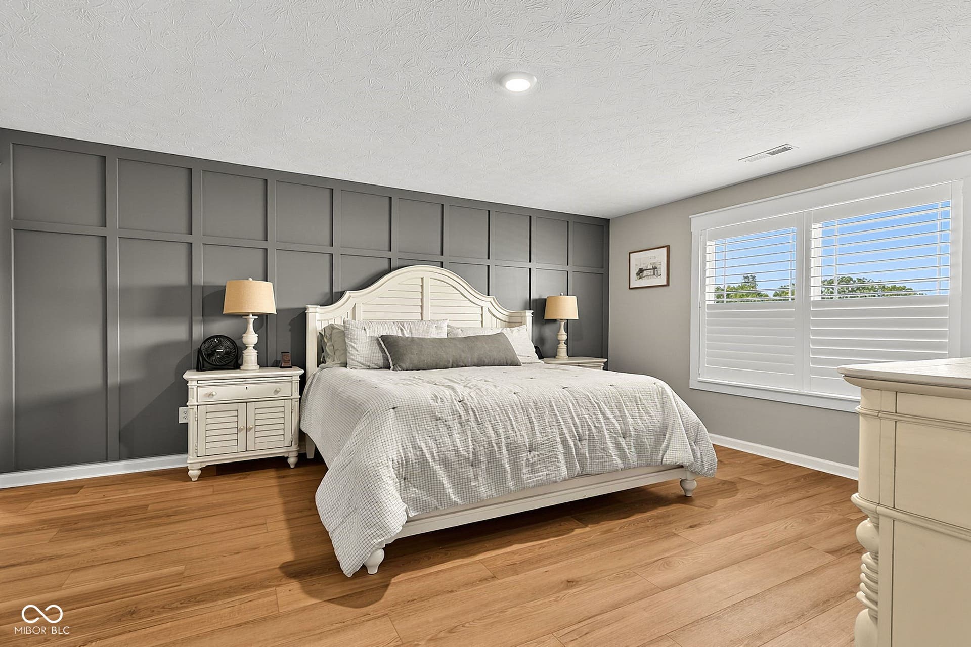 Wood-finish flooring, accent wall with panel molding, recessed lighting, and window with plantation shutters