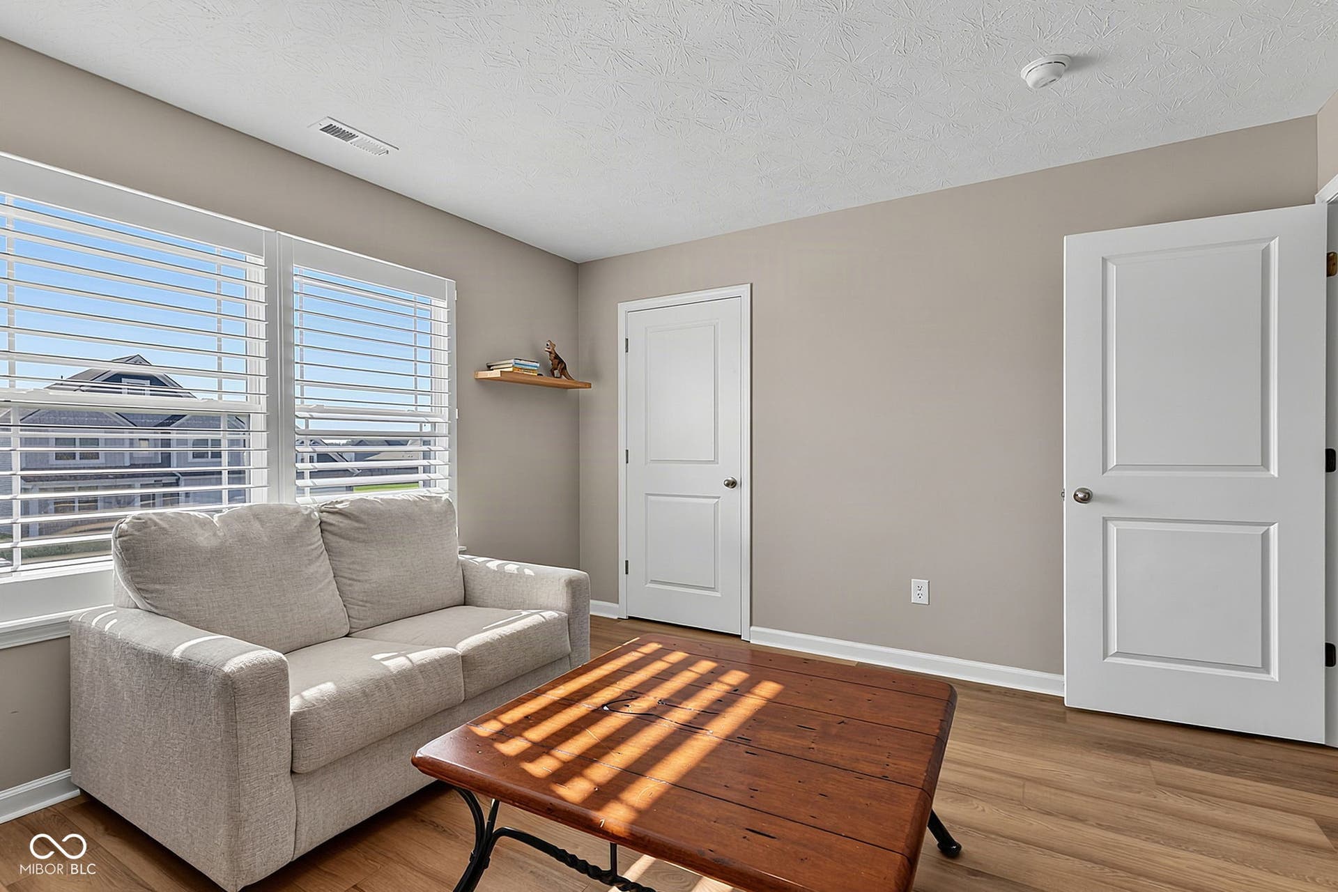 Wood-finish flooring, multiple windows with blinds, light neutral wall paint, and white paneled doors