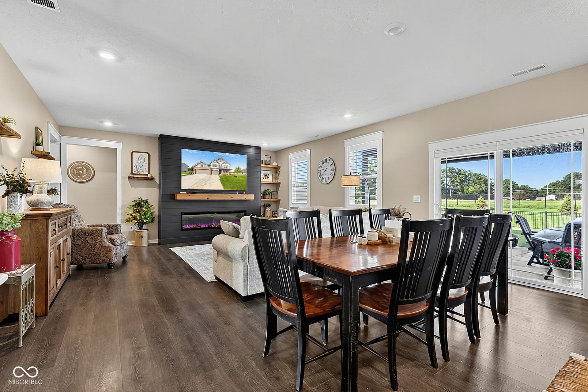 Open-concept living space featuring wood-finish flooring, a contemporary fireplace with shiplap surround, and built-in shelving