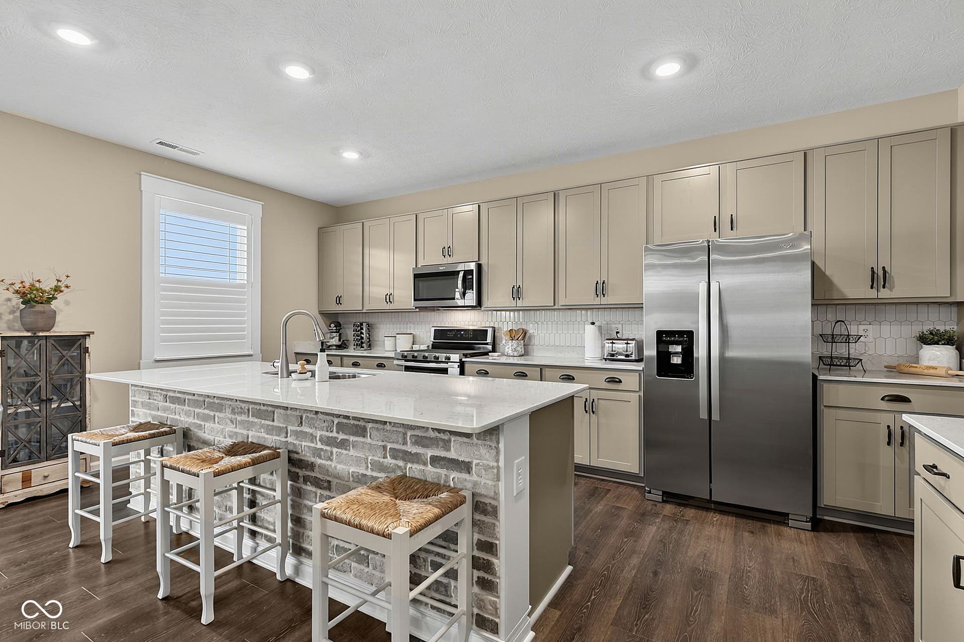 Spacious kitchen featuring an expansive island with brick-style detailing, light-toned cabinetry, stainless steel appliances, a white tile backsplash, and recessed lighting