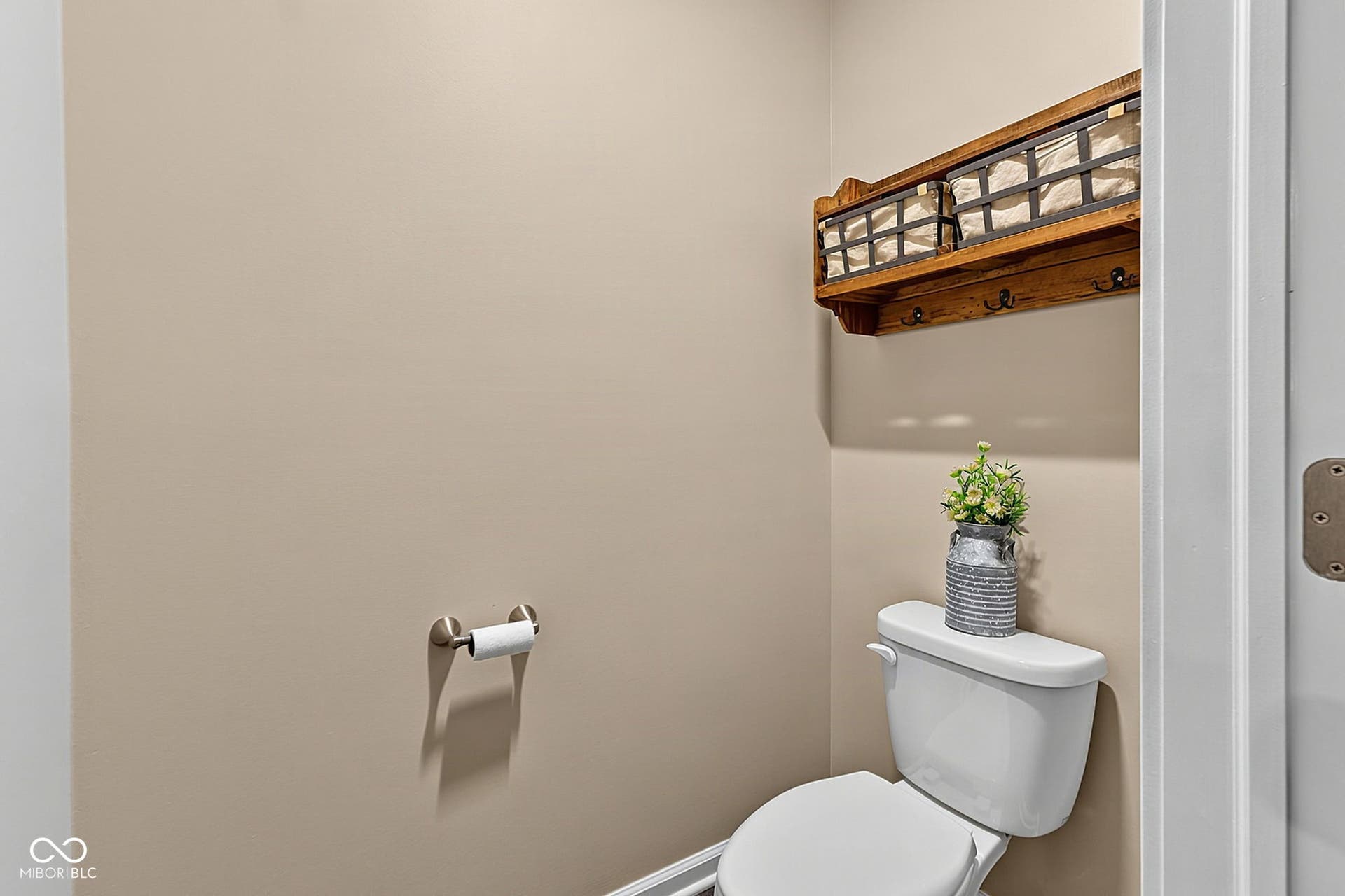 Wall-mounted wooden shelf with integrated hooks, neutral painted walls, and a white toilet