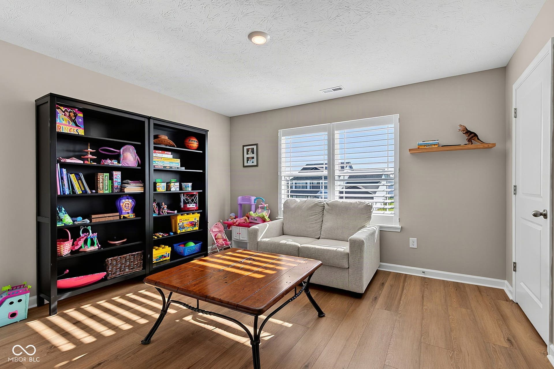 Recessed ceiling light, wood-finish flooring, two windows with blinds, built-in shelving, and a wall-mounted display shelf