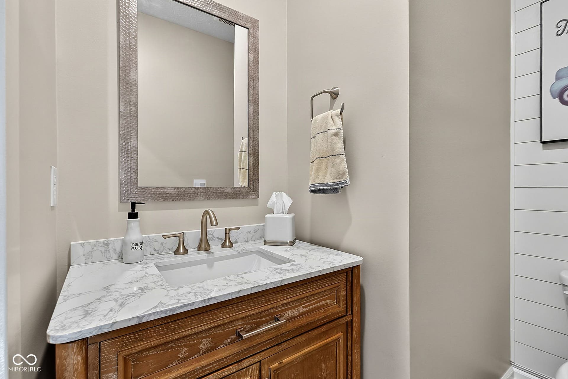 Bathroom vanity featuring a light-colored countertop with an integrated sink, a wood-finish cabinet with panel detailing, and a wall-mounted mirror with a textured frame