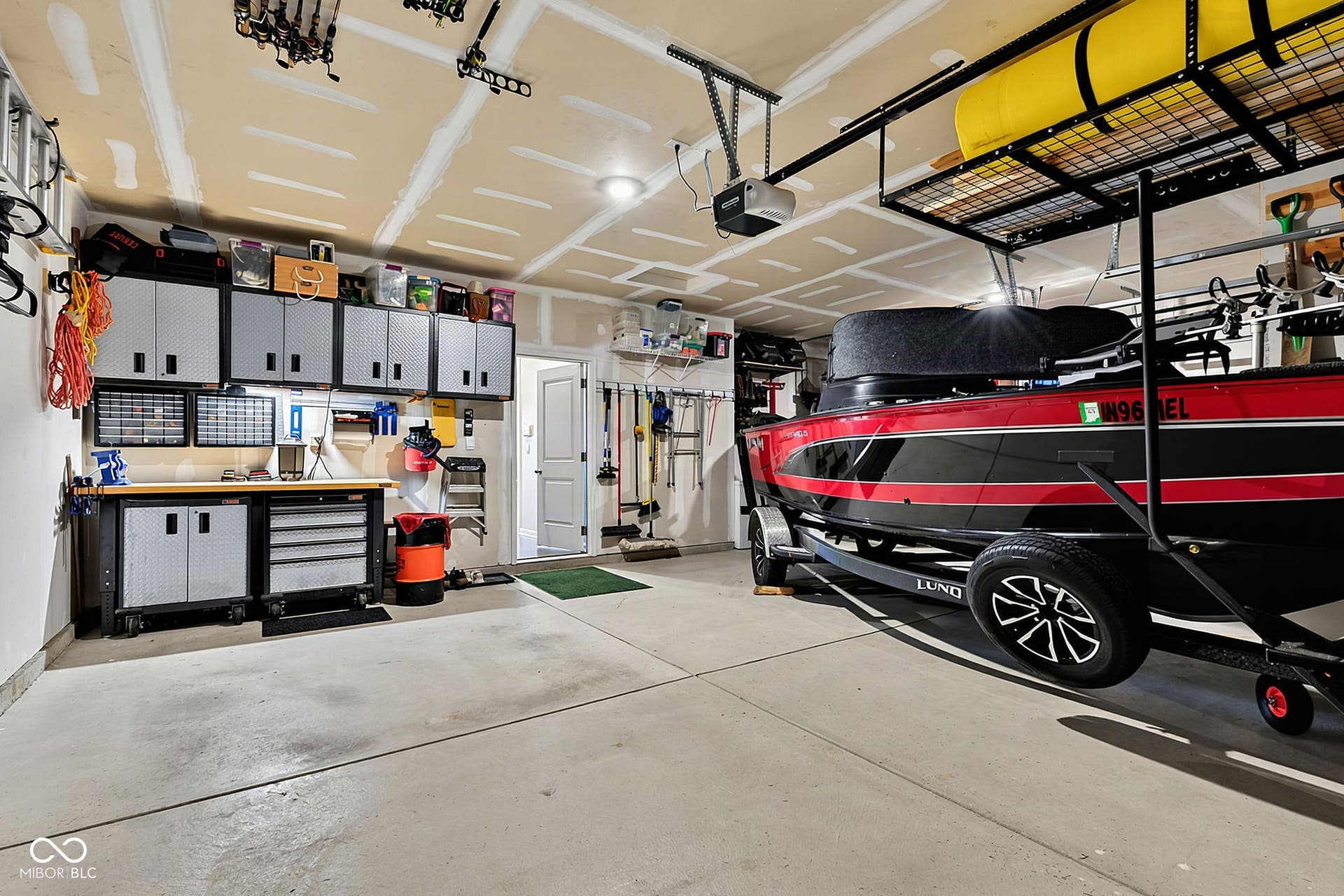 Spacious garage featuring a concrete floor, built-in overhead storage racks, integrated wall shelving, a workbench area, and a service door