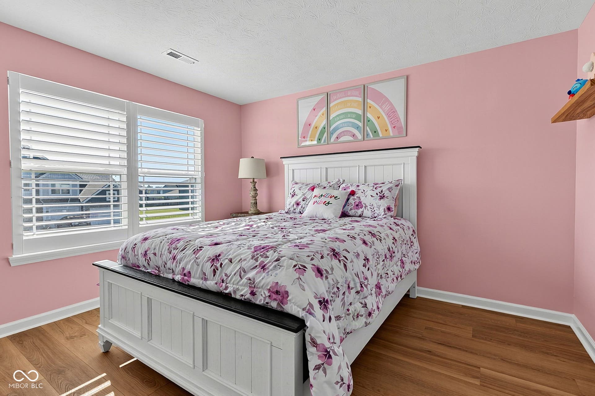 Wood-finish flooring with white trim, dual windows featuring plantation shutters, and a wall-mounted wooden shelf