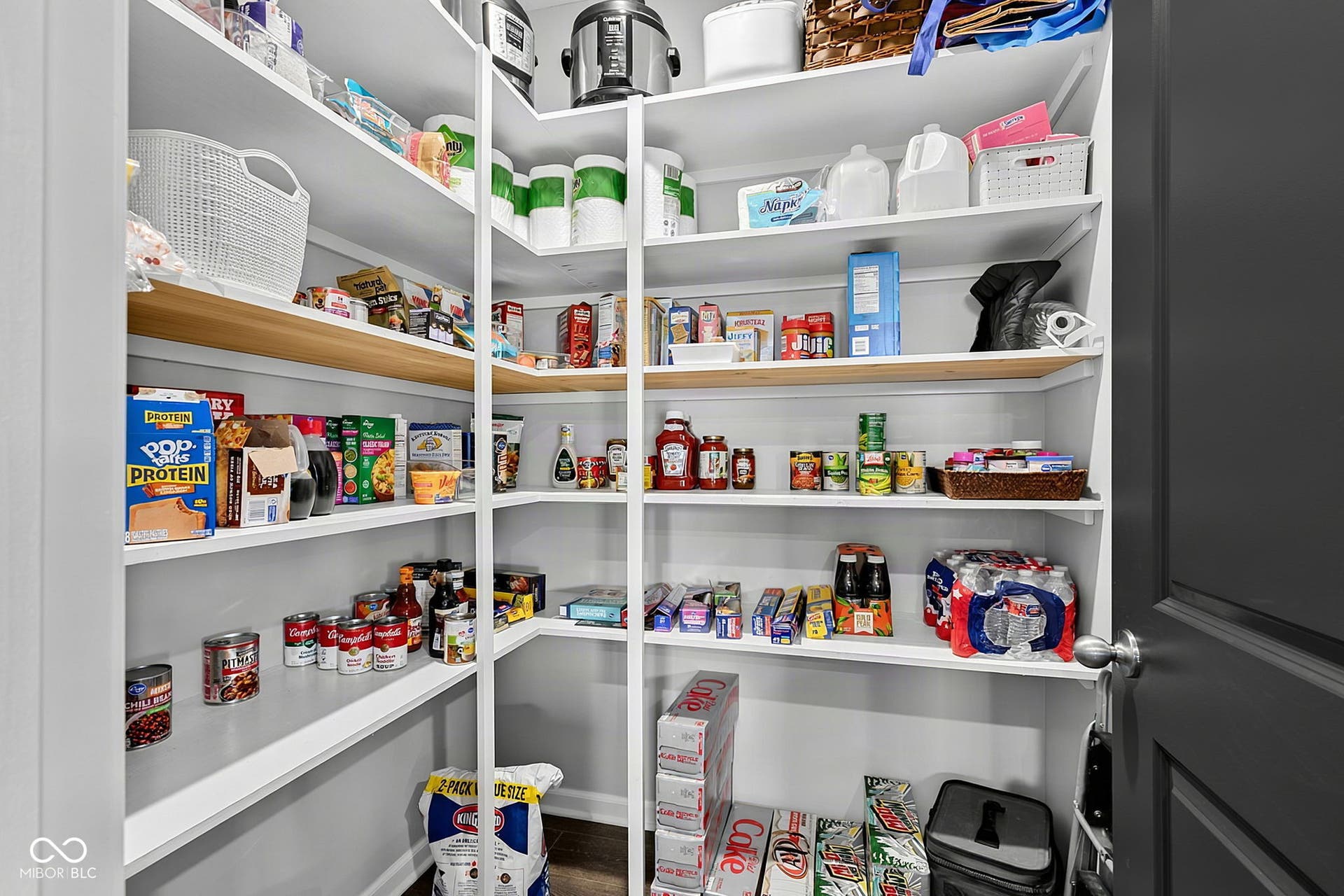 Spacious pantry featuring extensive built-in shelving, a mix of white and wood-finish shelves, and a dark paneled door