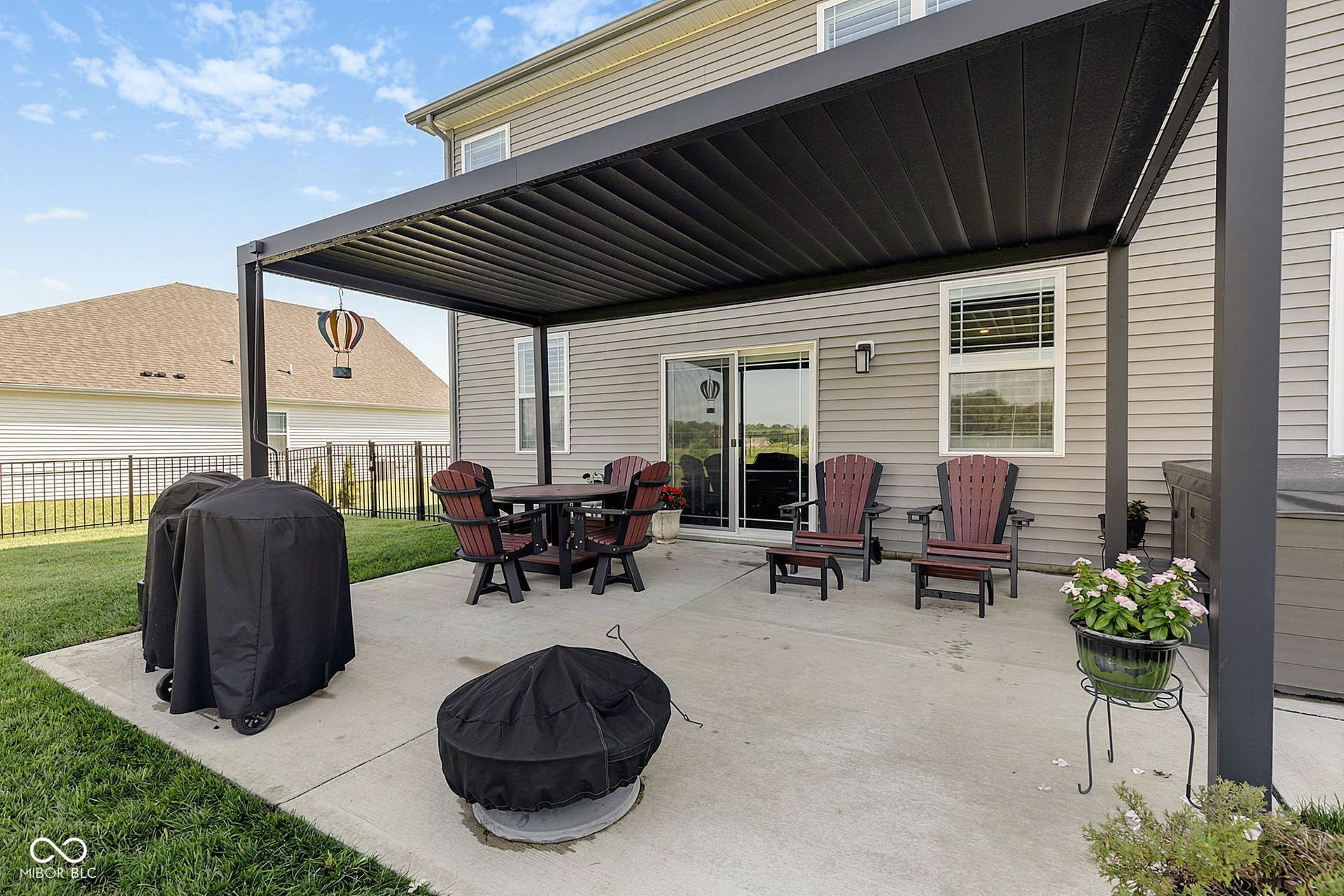 Concrete patio with a black louvered pergola, sliding glass door access, and exterior wall lighting