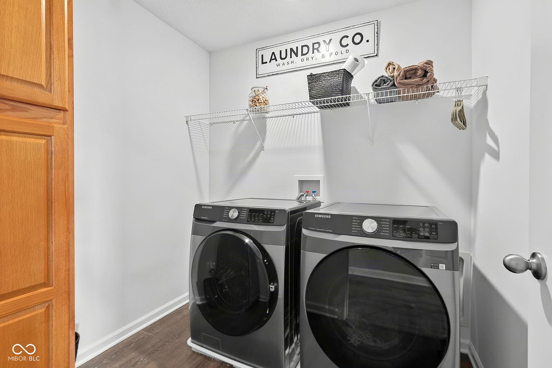 Integrated laundry area with wood-finish flooring, white walls, and a built-in wire shelf