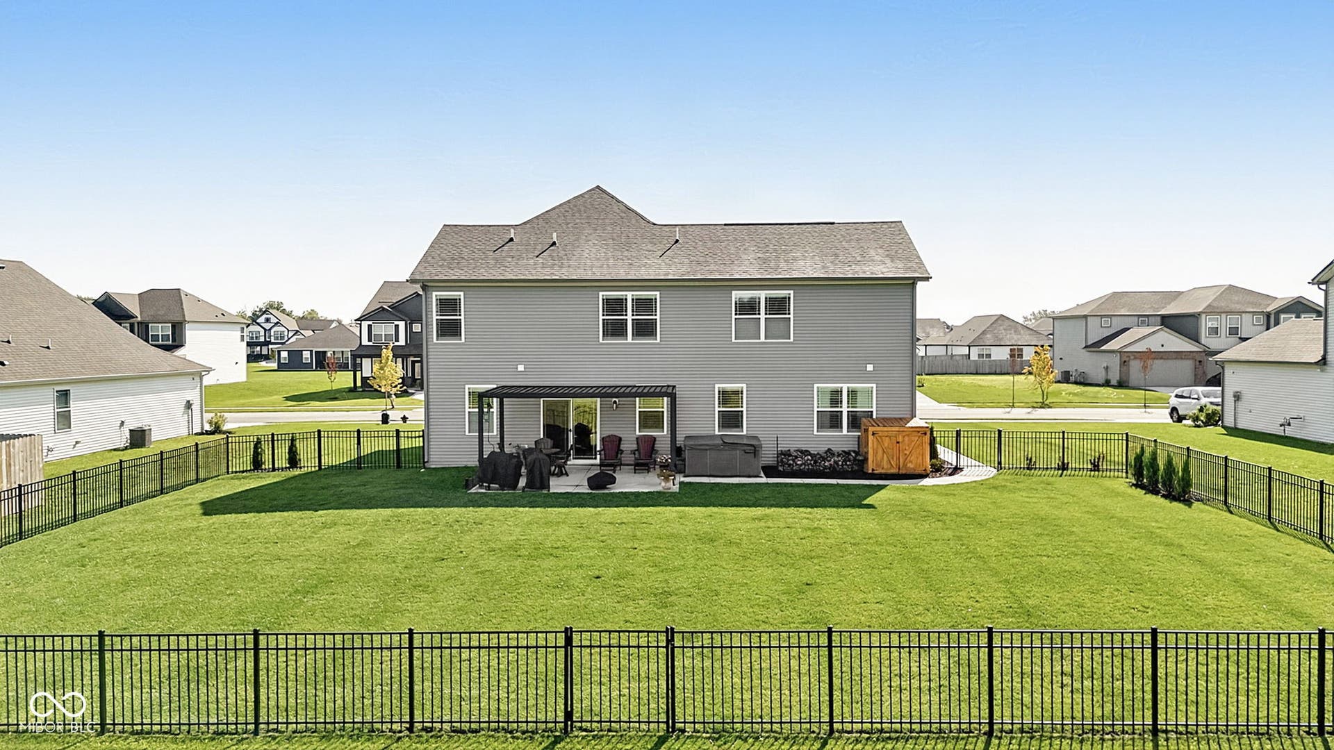 Expansive fenced backyard featuring a paved patio with a pergola, a built-in hot tub, and a storage shed