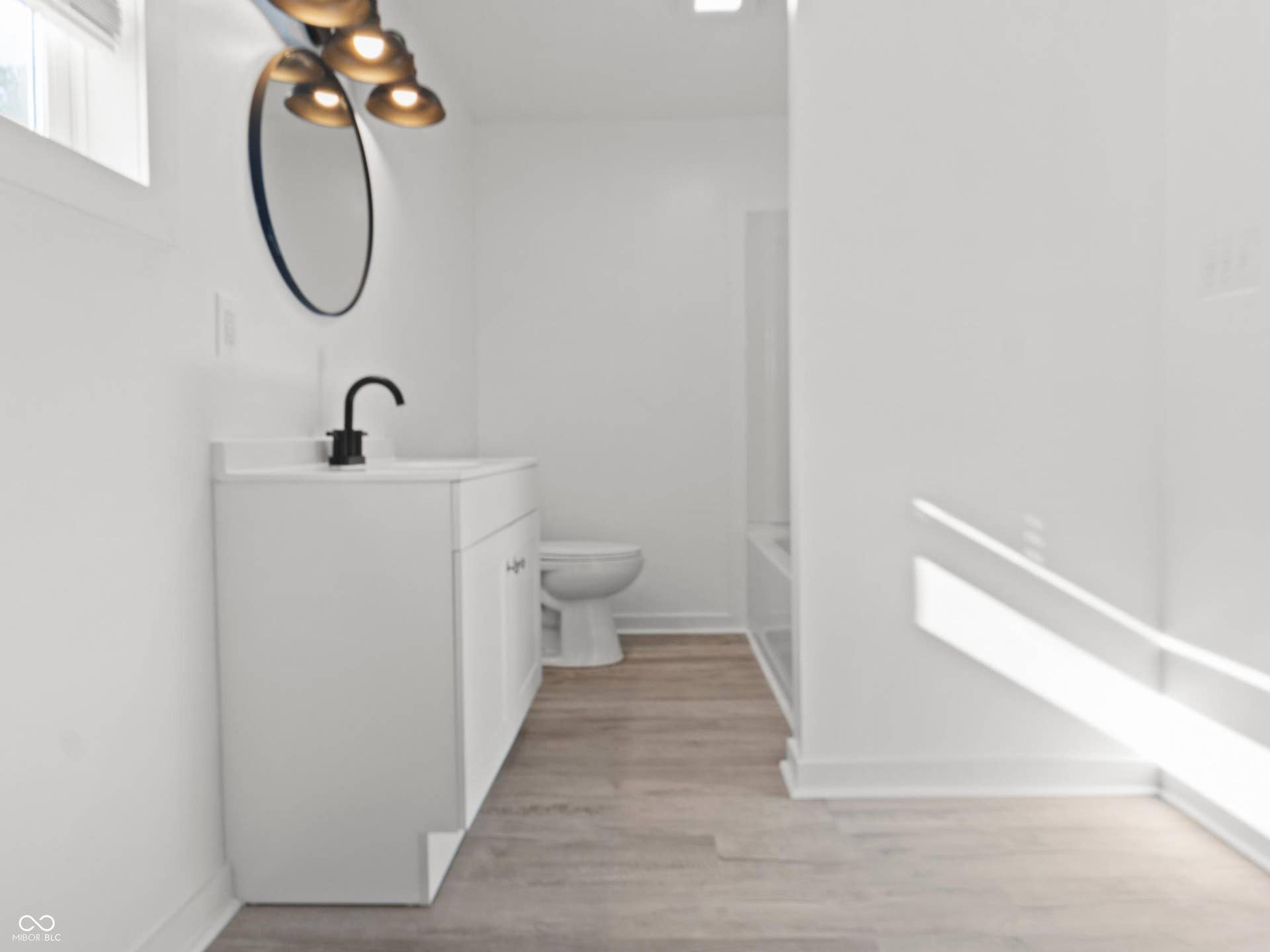 White vanity with integrated sink, black matte faucet, circular mirror, and multi-light fixture
