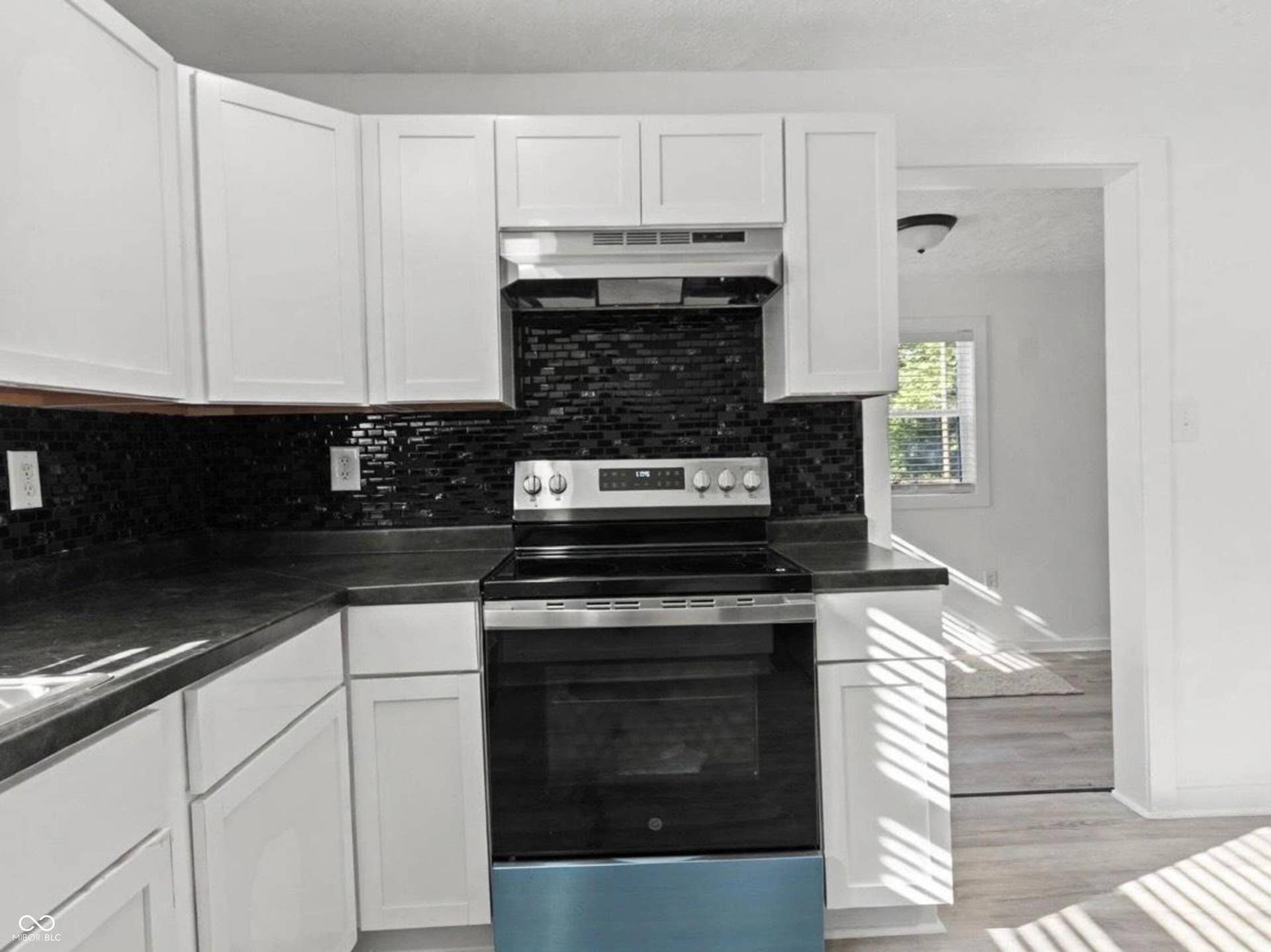 White shaker-style cabinetry, dark backsplash, dark countertops, and stainless steel appliances