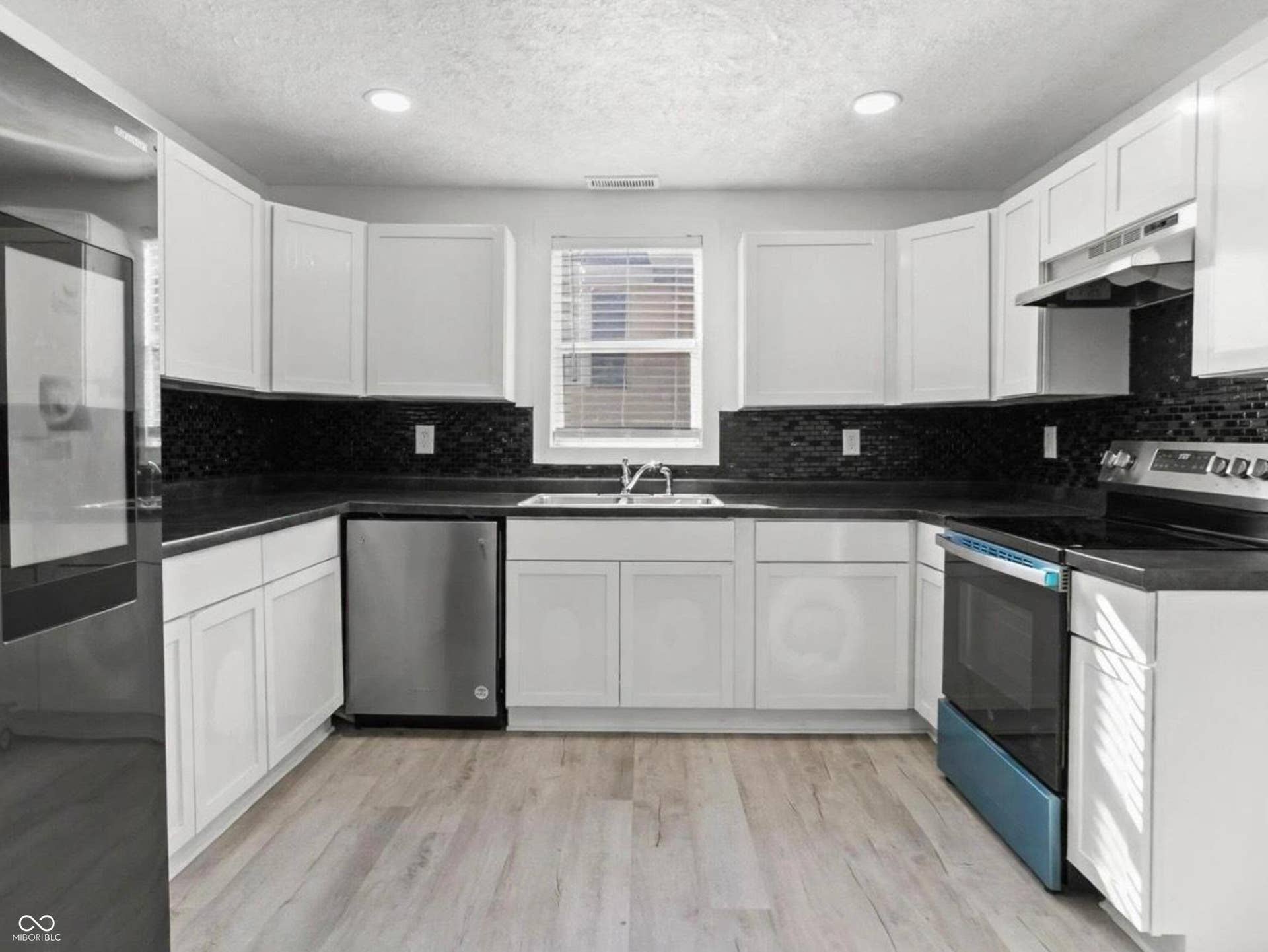 U-shaped kitchen with white cabinetry, dark countertops, black mosaic tile backsplash, and stainless steel appliances