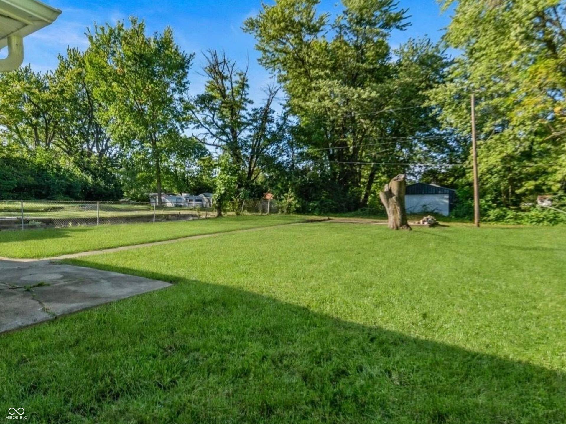 Expansive green lawn with mature trees and a concrete patio area