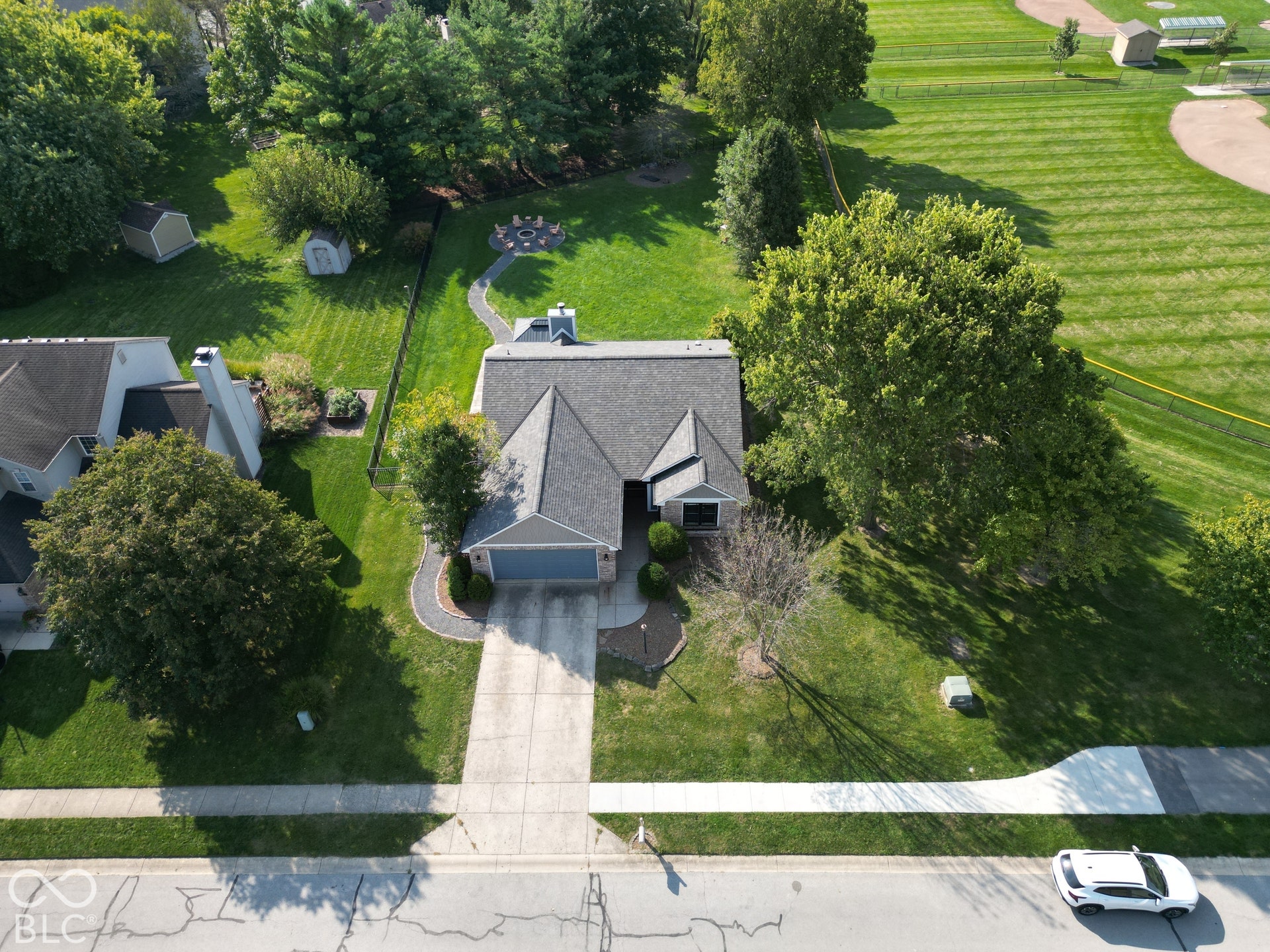 Gabled roofline with dark shingles, paved driveway, attached garage, curved paver pathway, and extensive green space