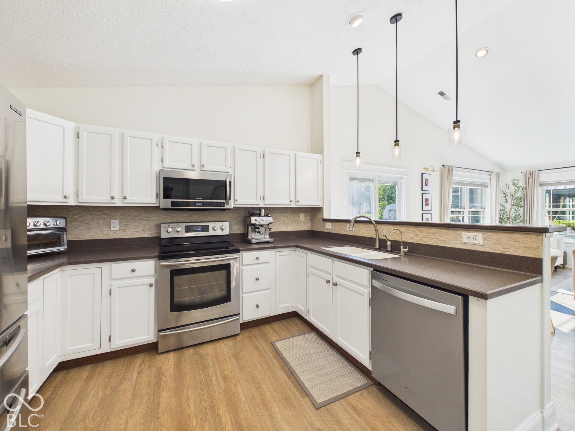 Kitchen featuring white cabinetry, stainless steel appliances, wood-finish flooring, and a vaulted ceiling