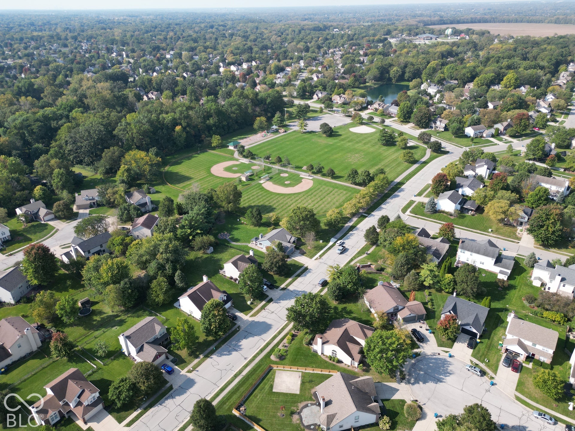 Expansive green spaces with two baseball diamonds, mature trees throughout the neighborhood, and a visible body of water